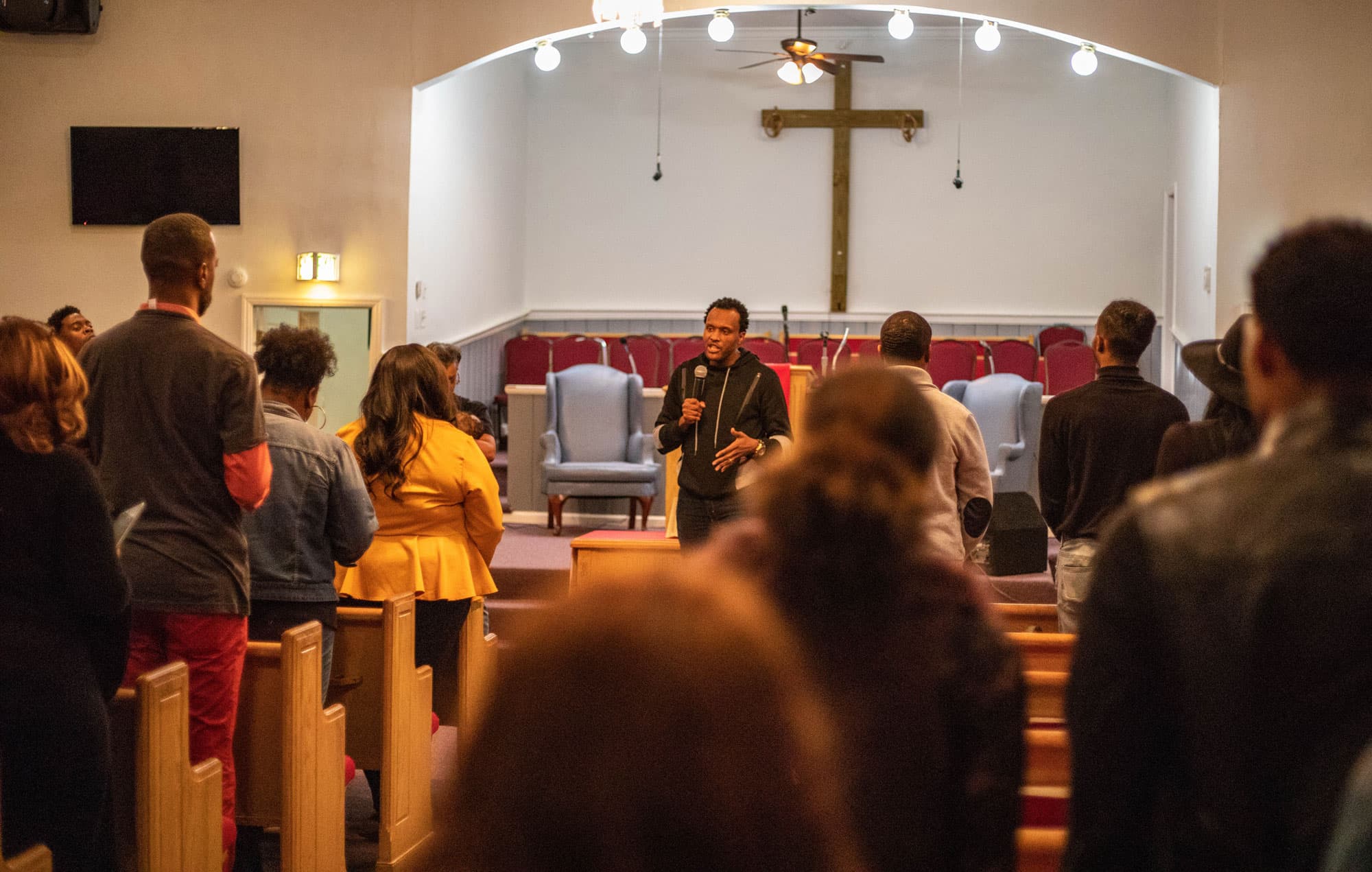 Rev. Antonio Grissom is shown speaking with a microphone in hand to a group of people at the Chapel Hill Baptist Church.