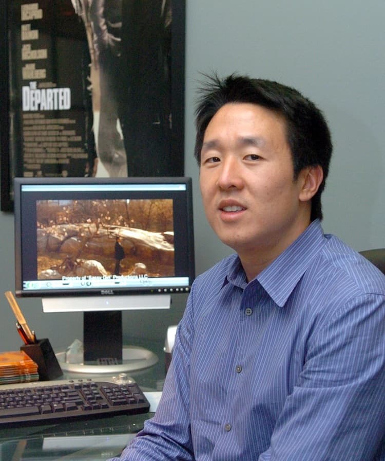 Man sitting at computer that is rendering film scene, with movie poster for "The Departed" behind