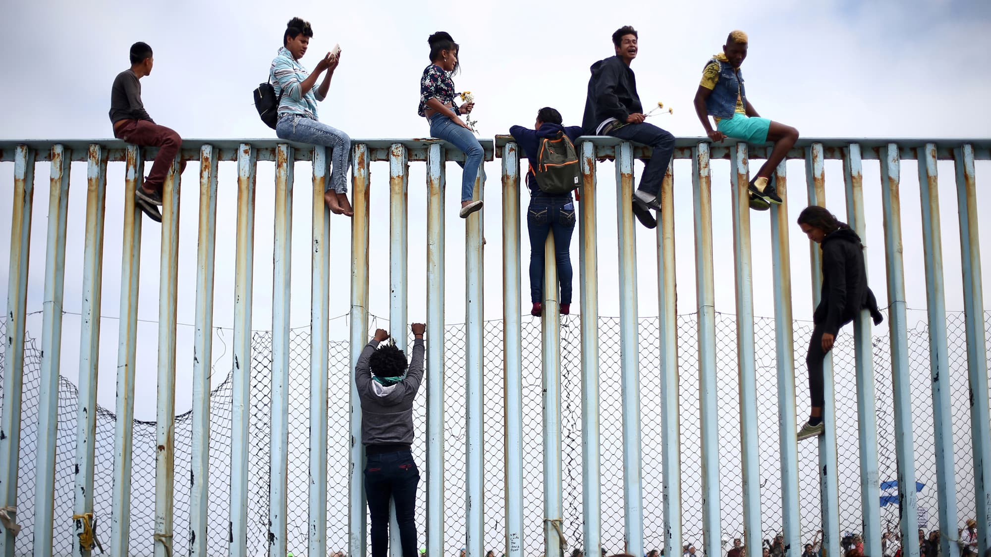 People sit on a fence with a blue sky behind them.