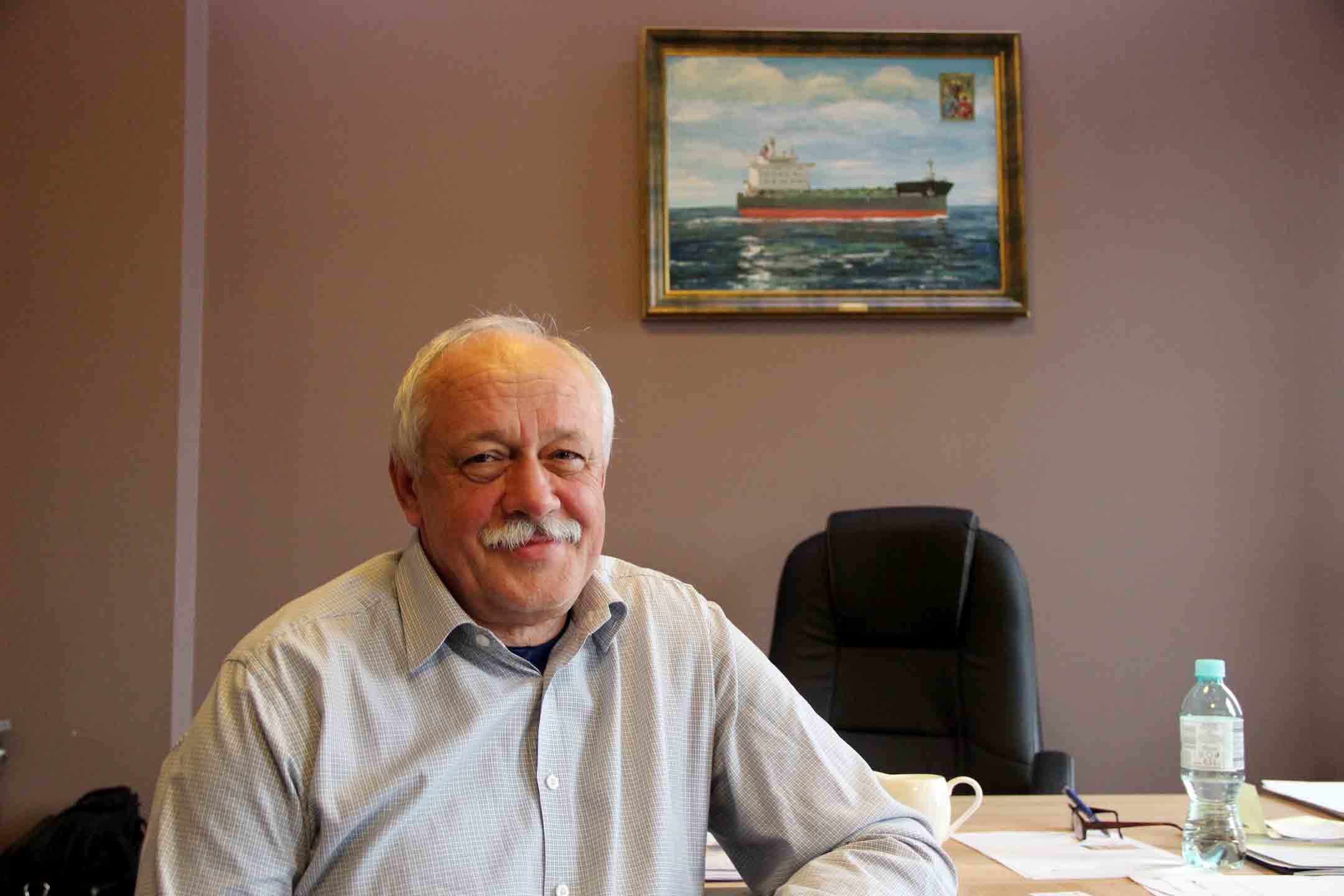 A man with white hair sits at a desk.