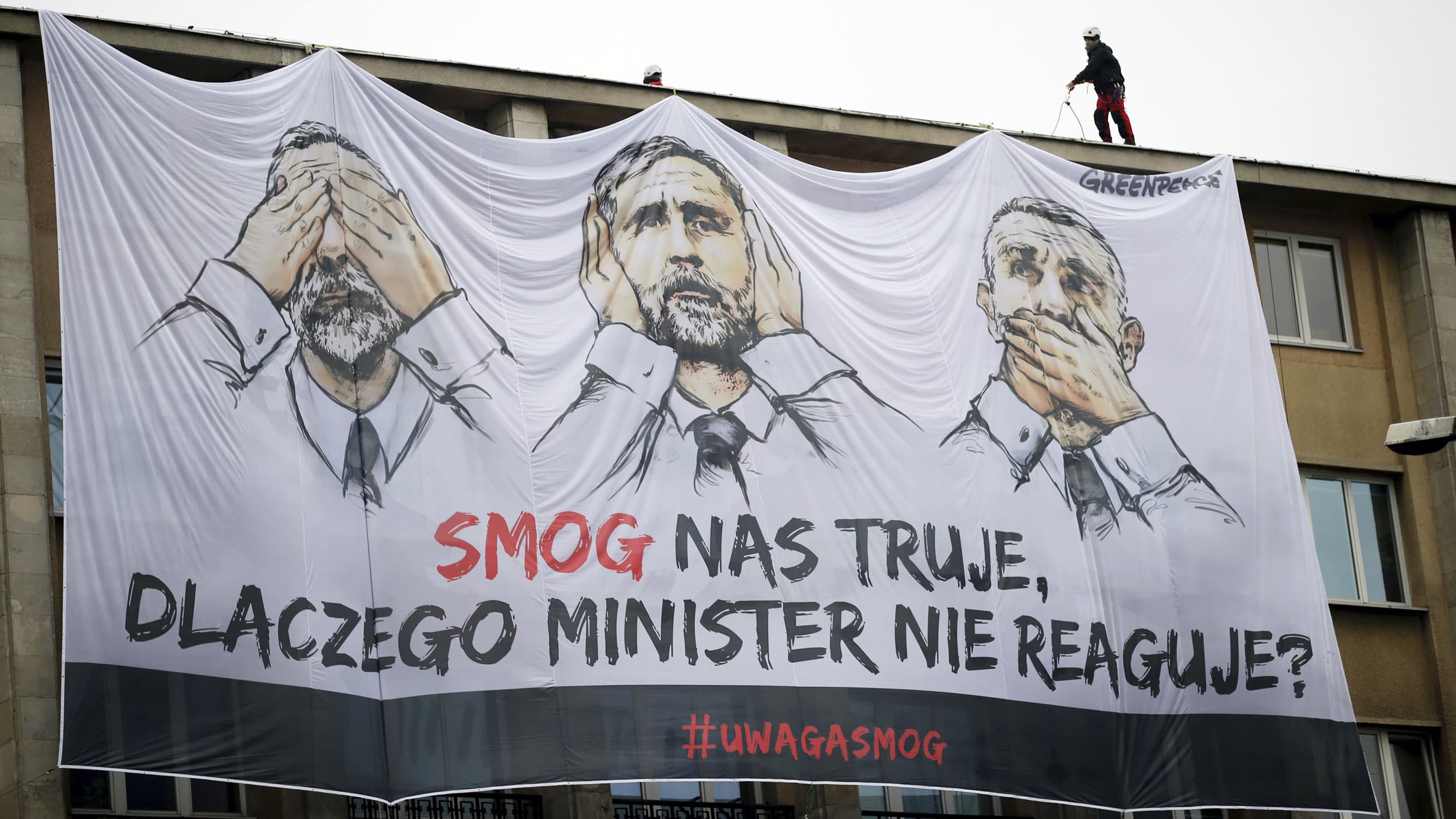 a large banner hangs from a government building with cartoon images of a politician with his eyes, ears and mouth covered.