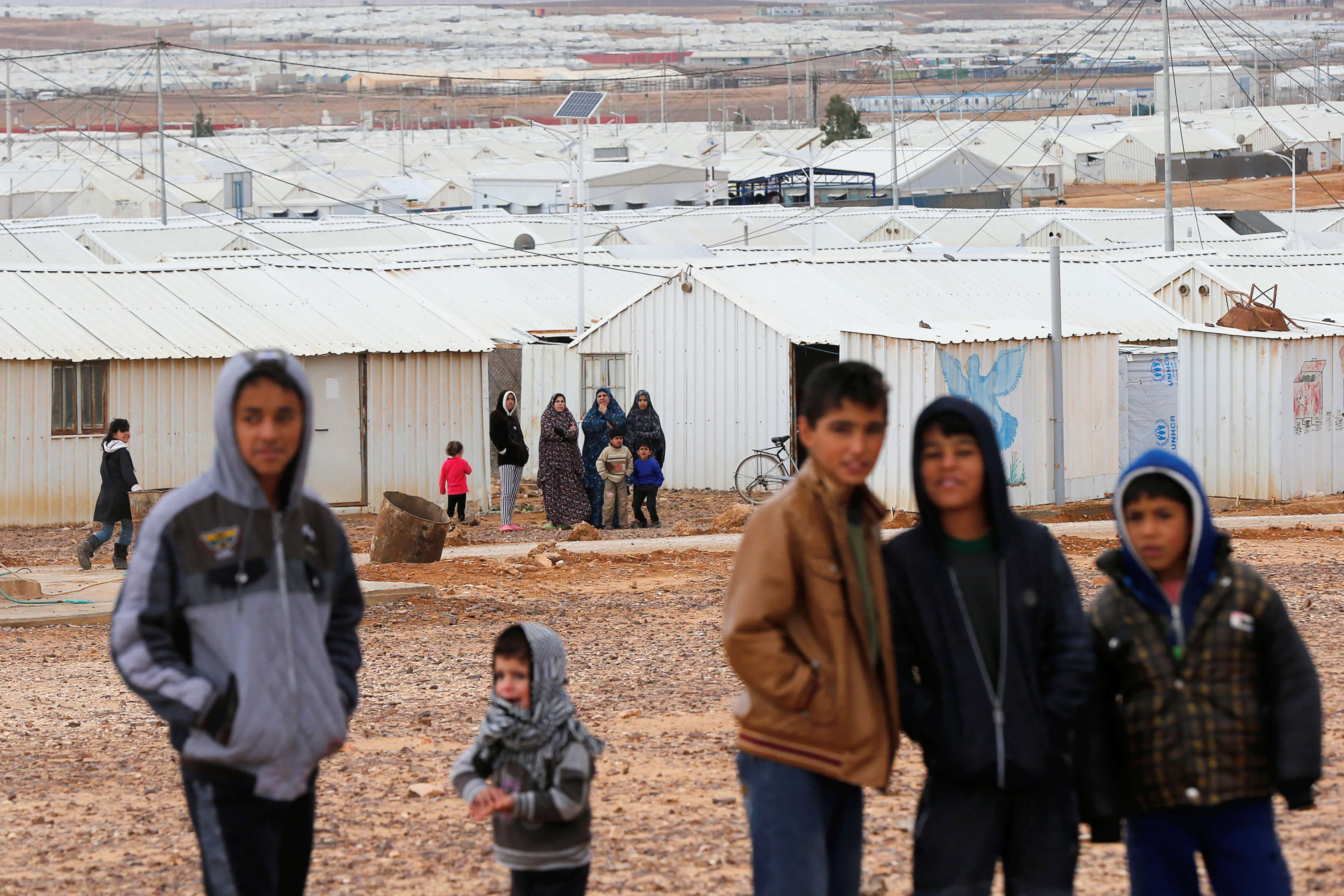 Syrian refugees look at the camera as they stand in front of their homes at Azraq refugee camp