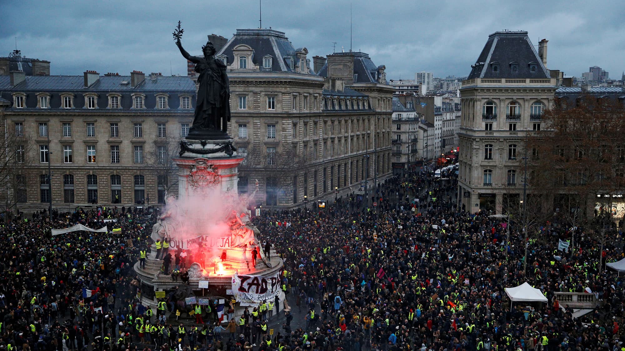 The Place de la République in Paris is shown in the background with thousands encircling a monument in the middle of the square.