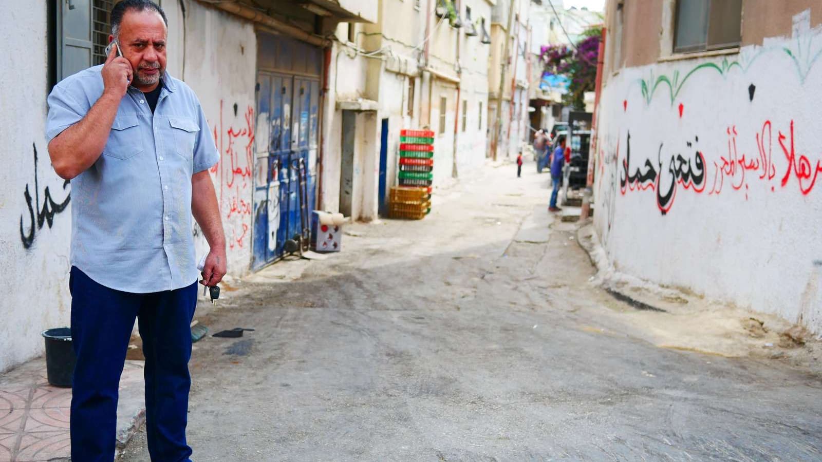 A man wearing a blue shirt and jeans walks on the street with his phone near his ear.