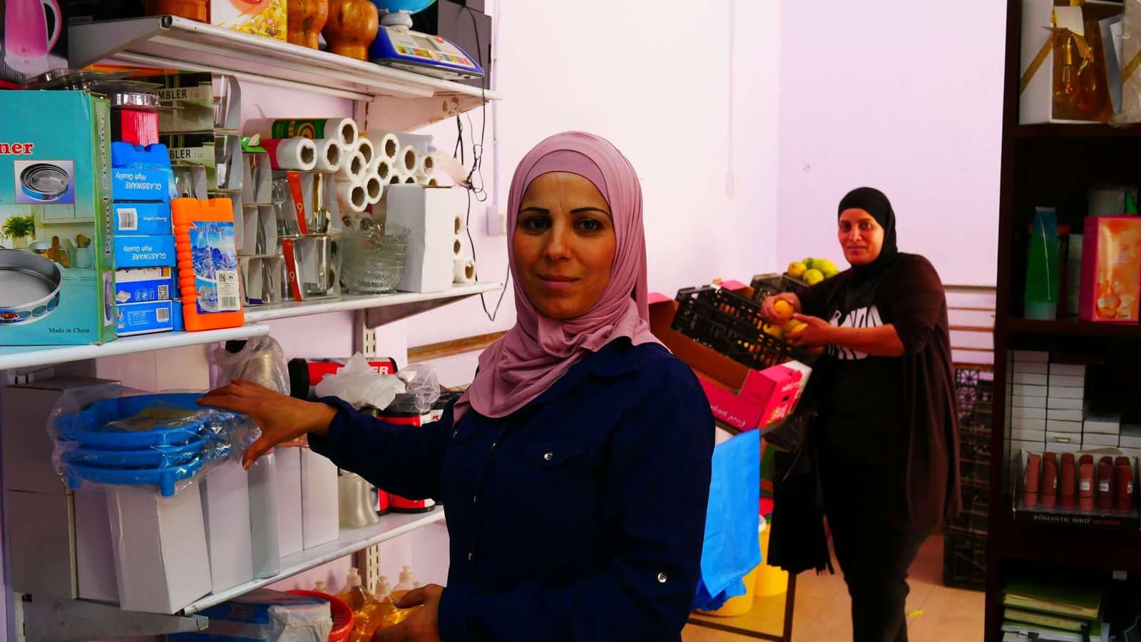 Two women stand in a shop and look at the camera.