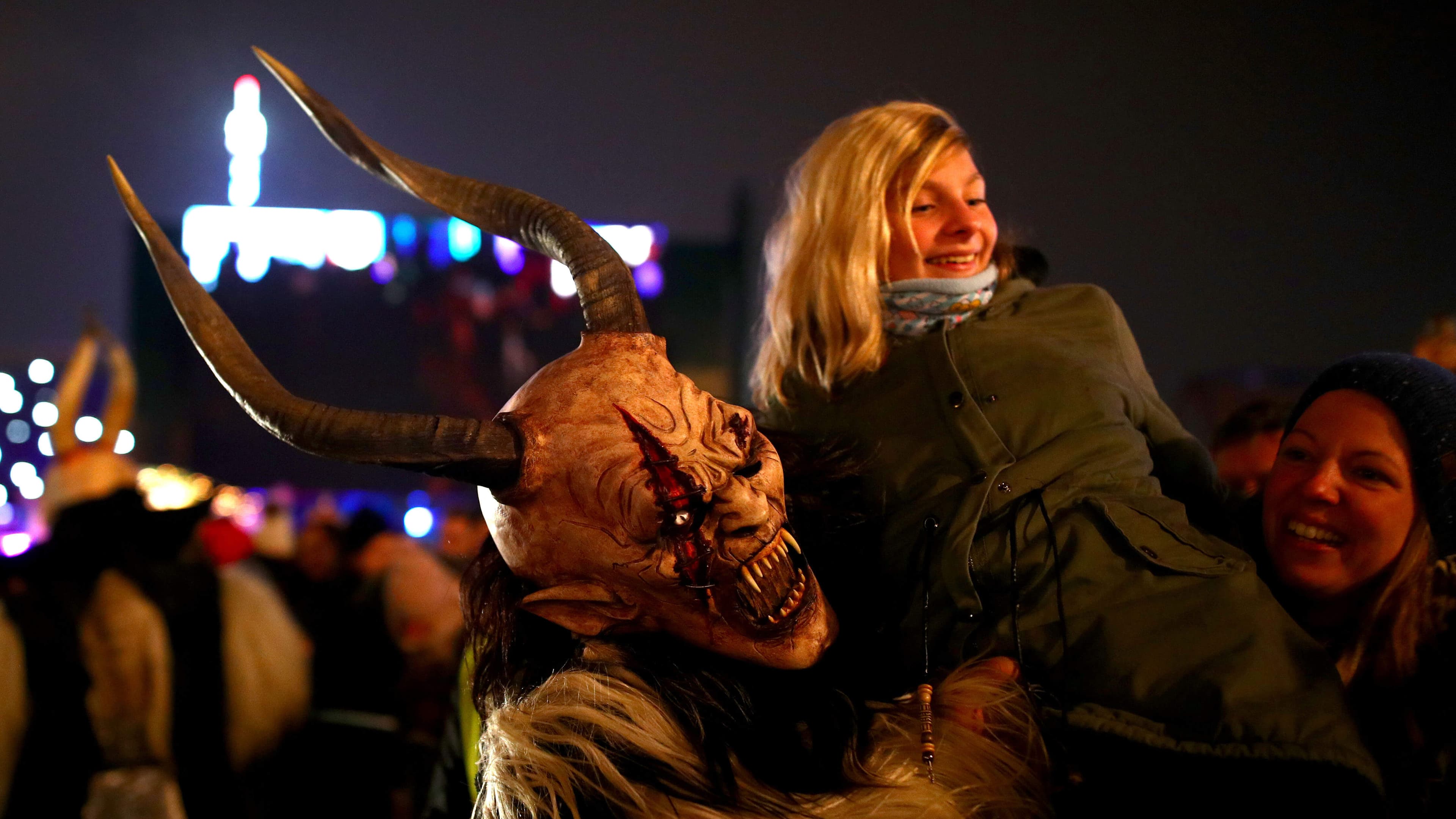 a person wearing a costume of horns, fangs and fur, carries a woman over their shoulder