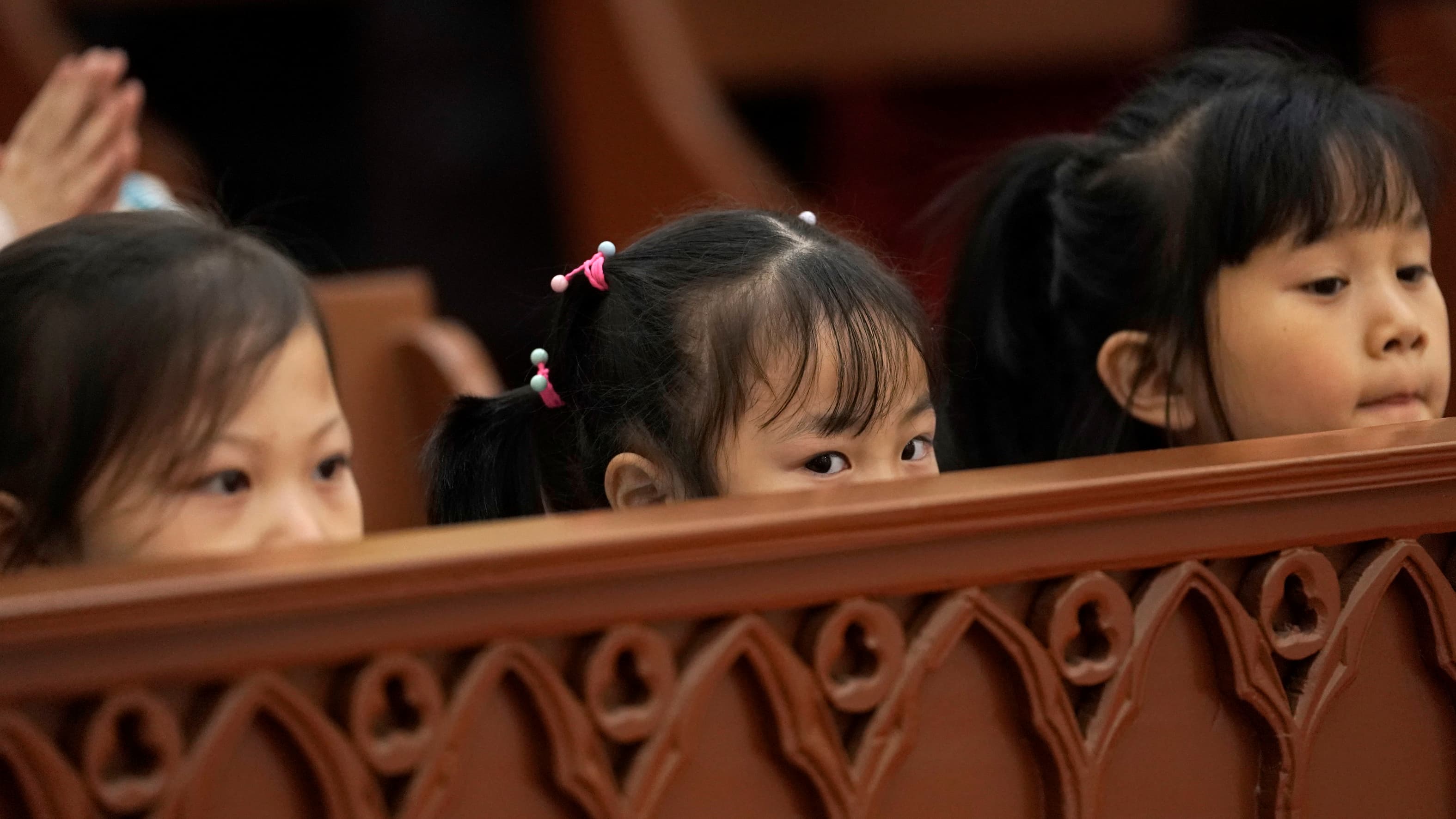 Three girls peer over the pew in church in China.