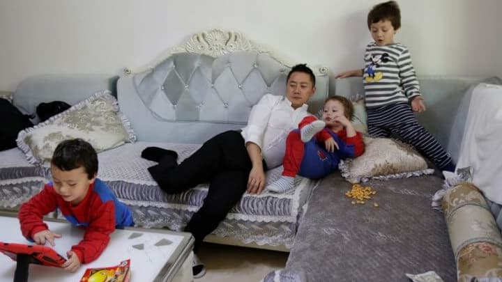 A father rests on the sofa with this three sons in China.