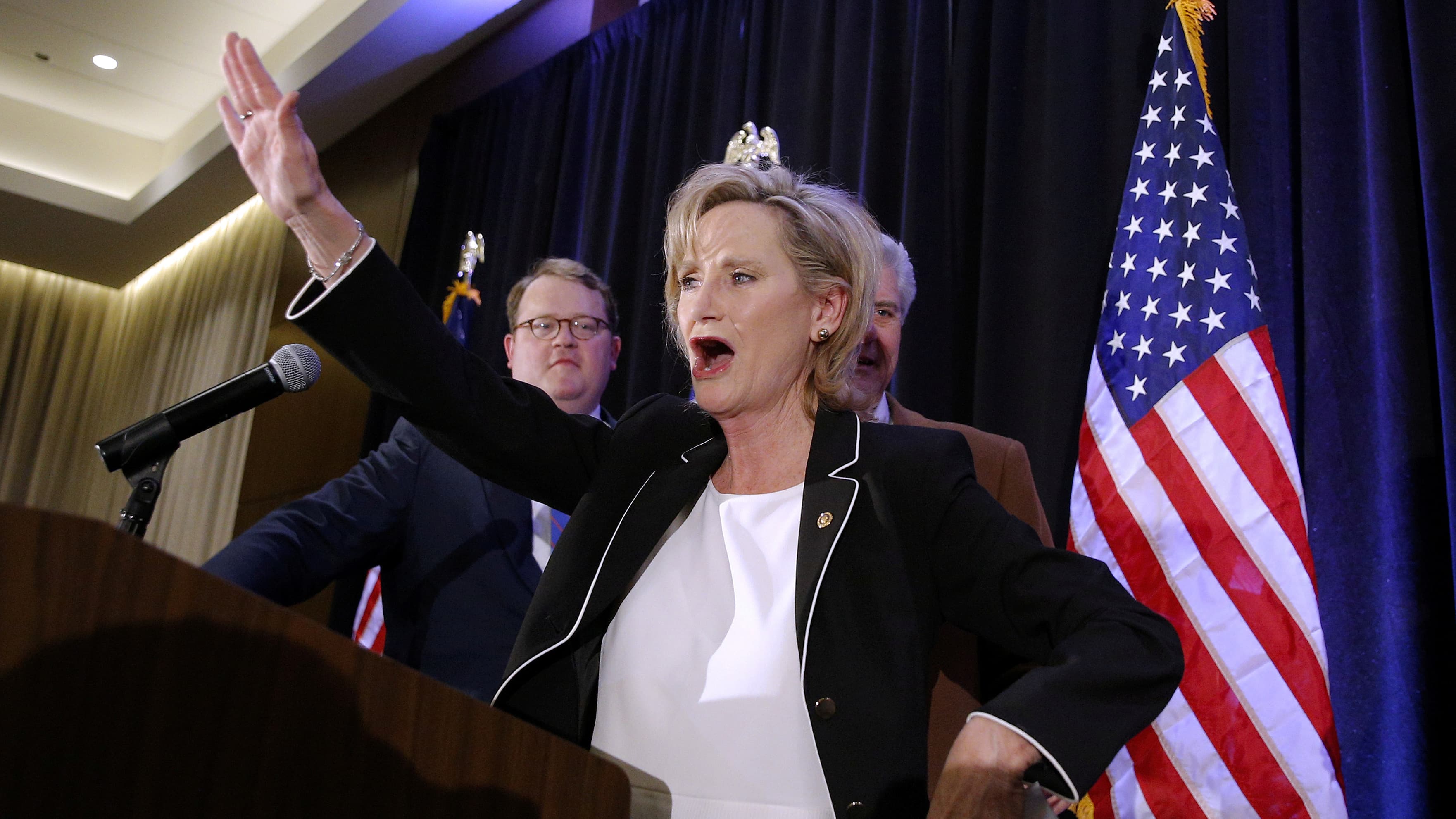 Republican US Senator Cindy Hyde-Smith raise her arm up at the podium on election night.