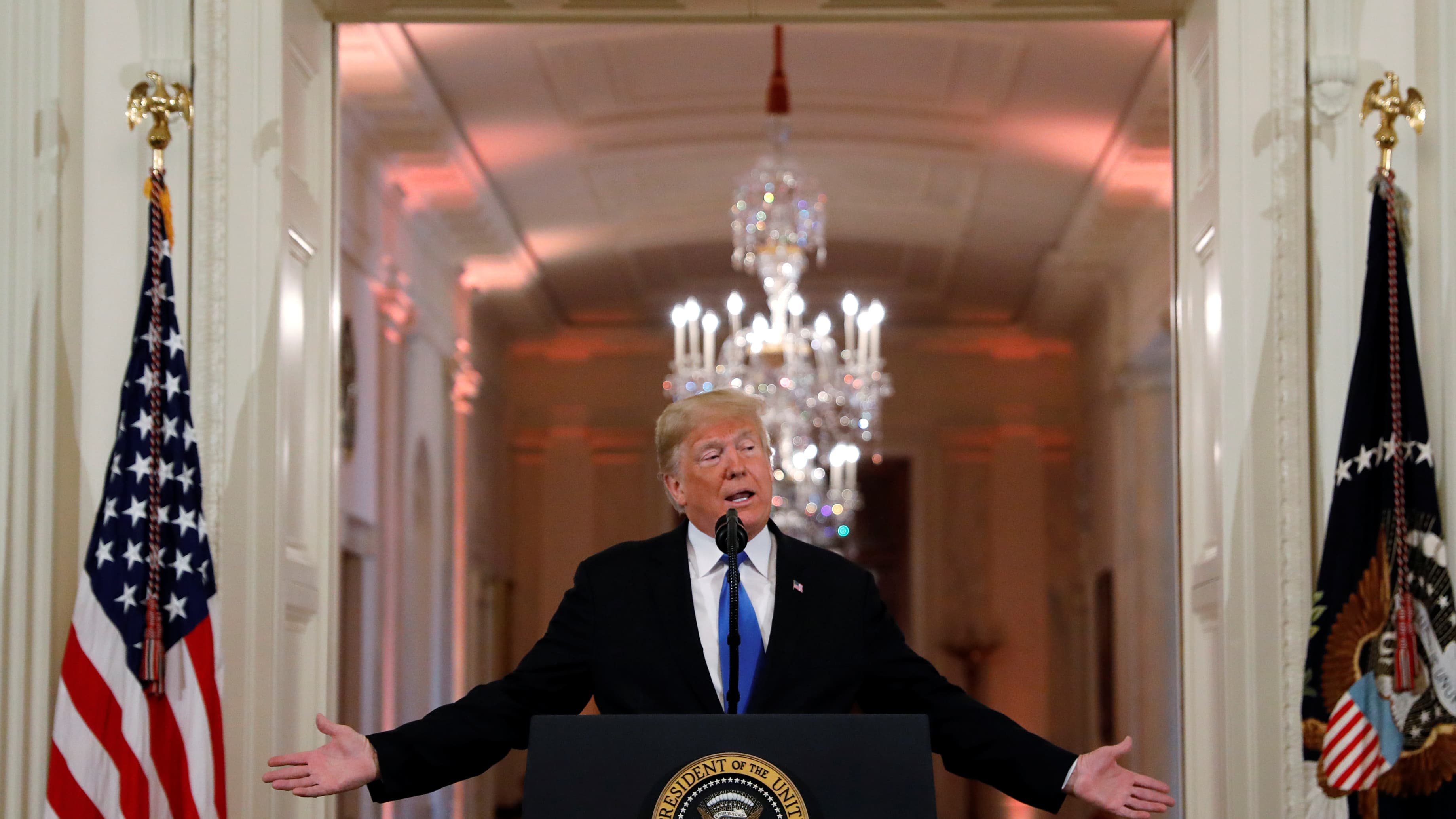 Donald Trump speaks at podium flanked by two flags.
