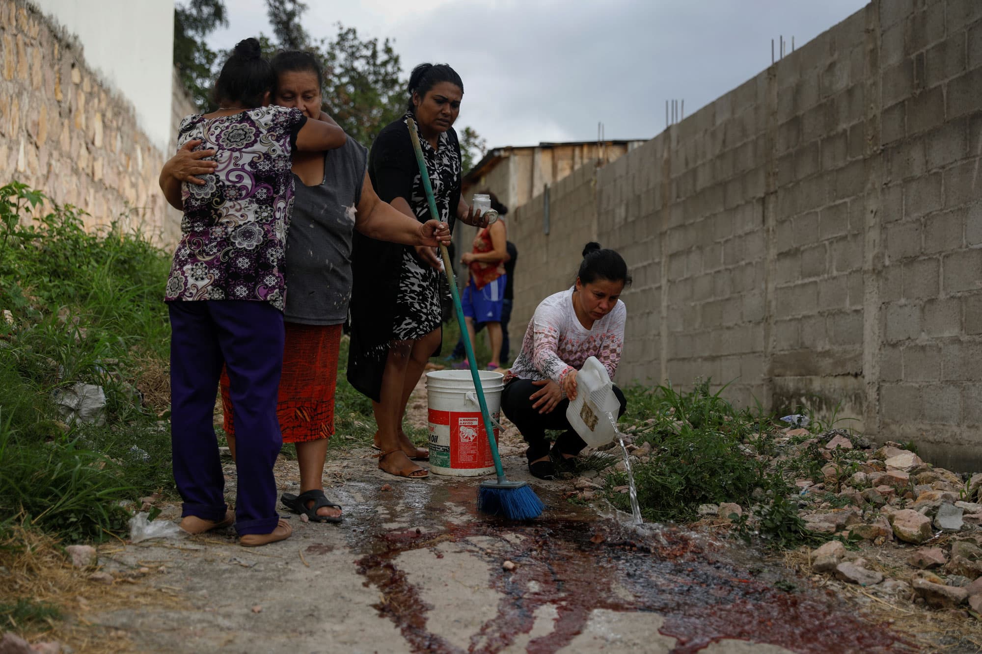 Relatives and friends of Ronald Blanco are shown in the street, a pair hugging and another wash the blood from the crime scene.