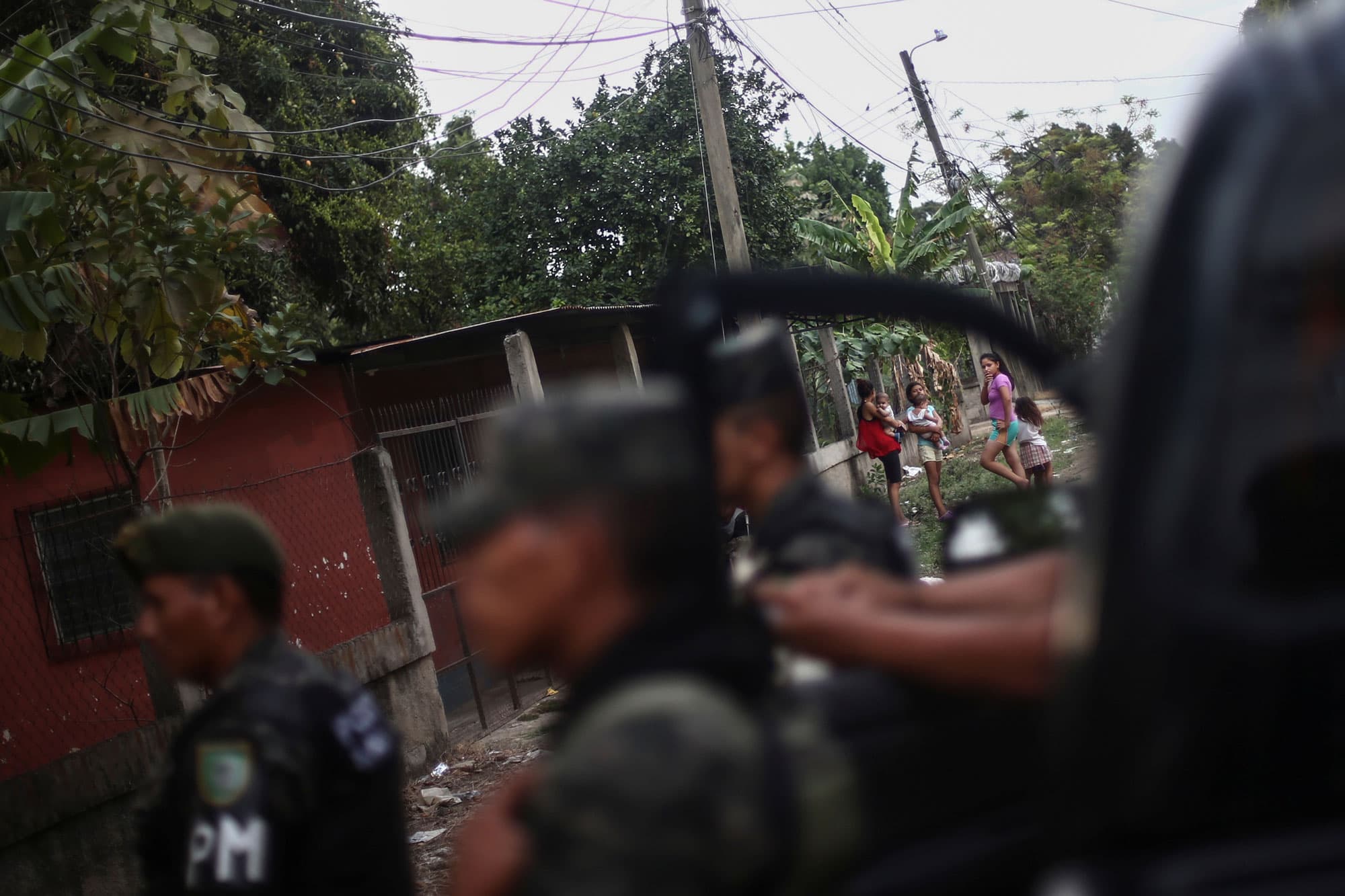 A group of children are shown in the distance looking toward a crime scene with police in te near ground in soft focus.