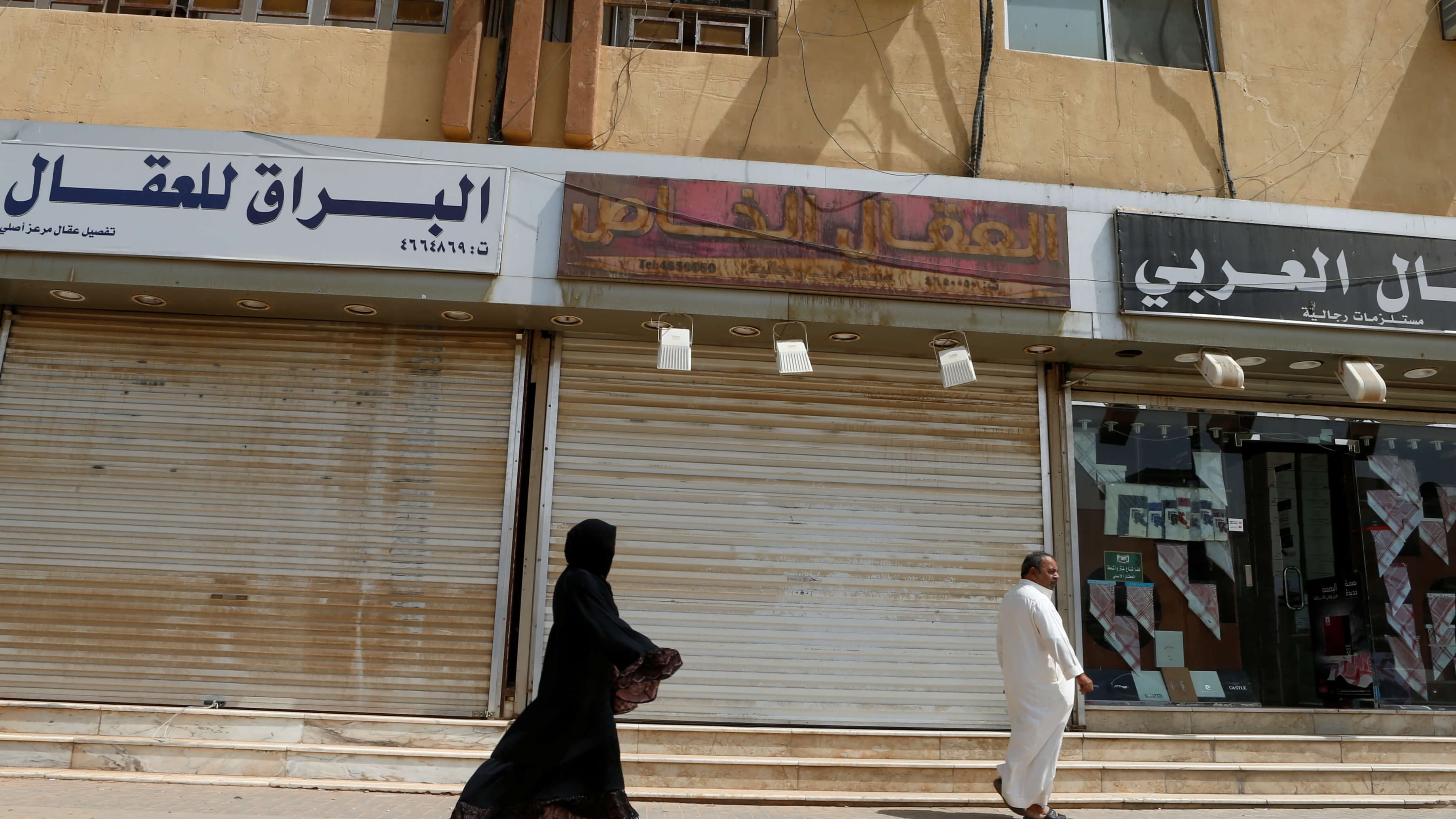 Saudi woman dressed in black robe walks behind a man wearing all white.