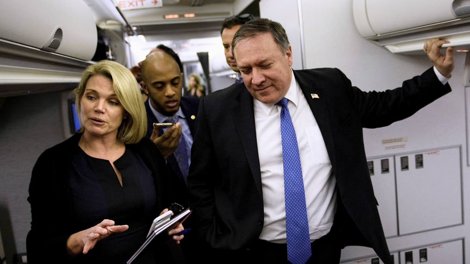 Heather Nauert and Mike Pompeo wear navy blue suits and speak with reporters inside a plane.