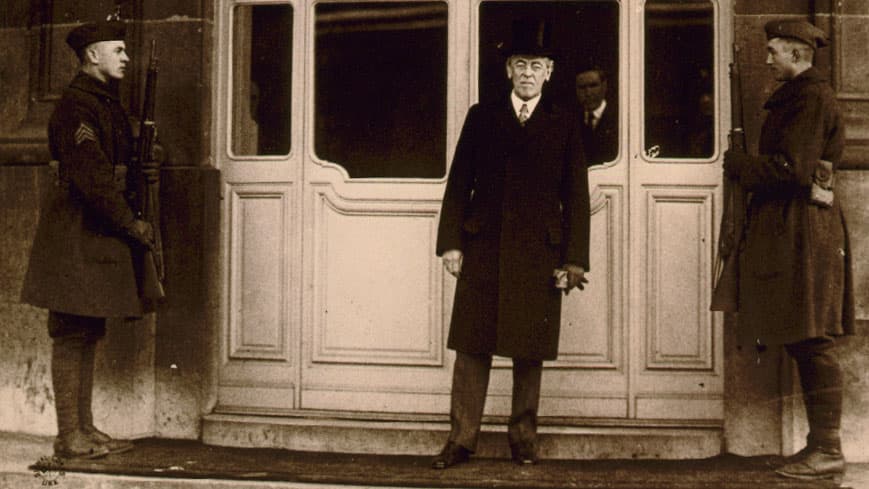 President Woodrow Wilson stands in front of a large window flanked by two soliders