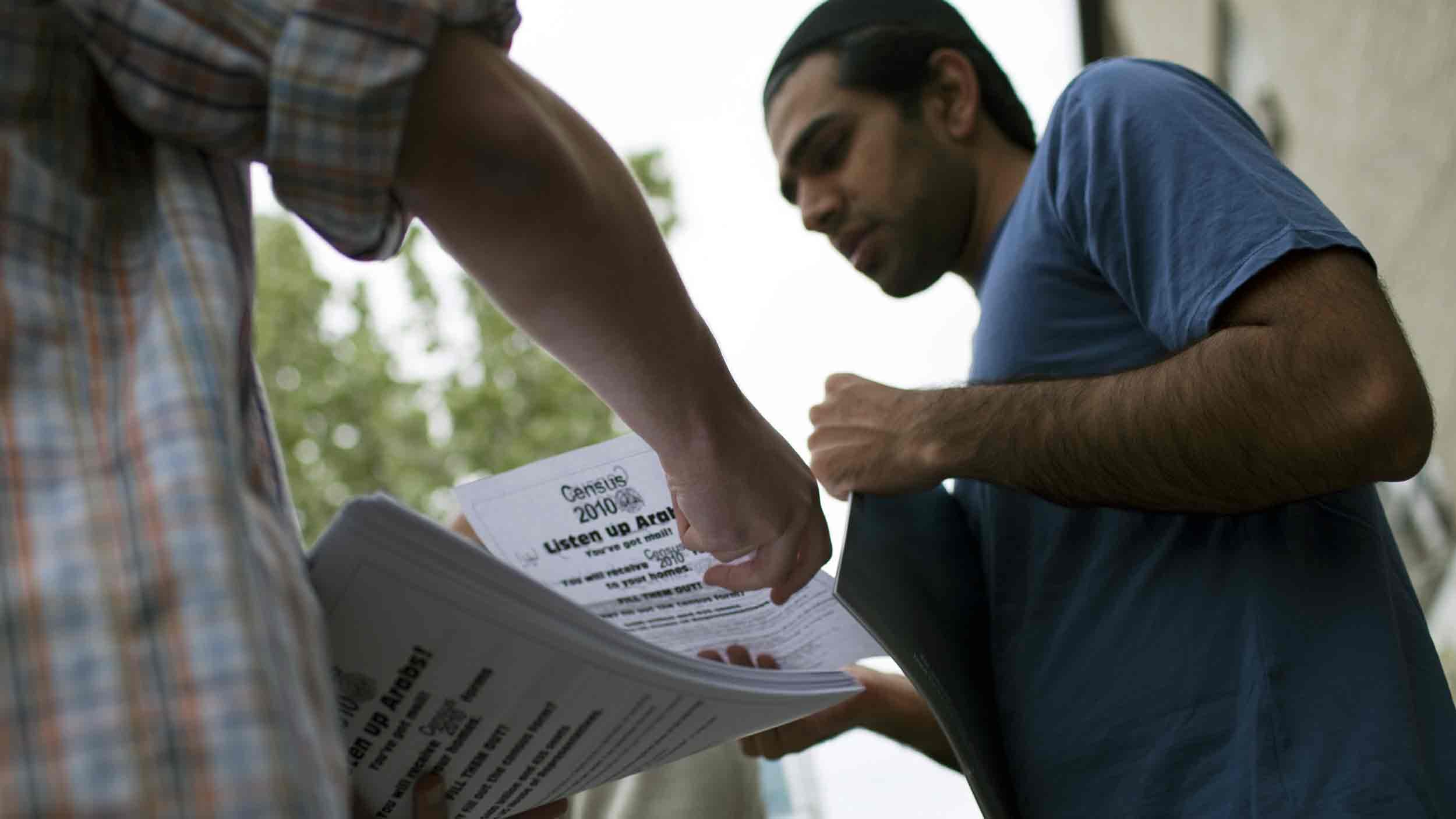 A man is being handed a flier that says "Listen up Arabs" and describes the Census 2010 process.
