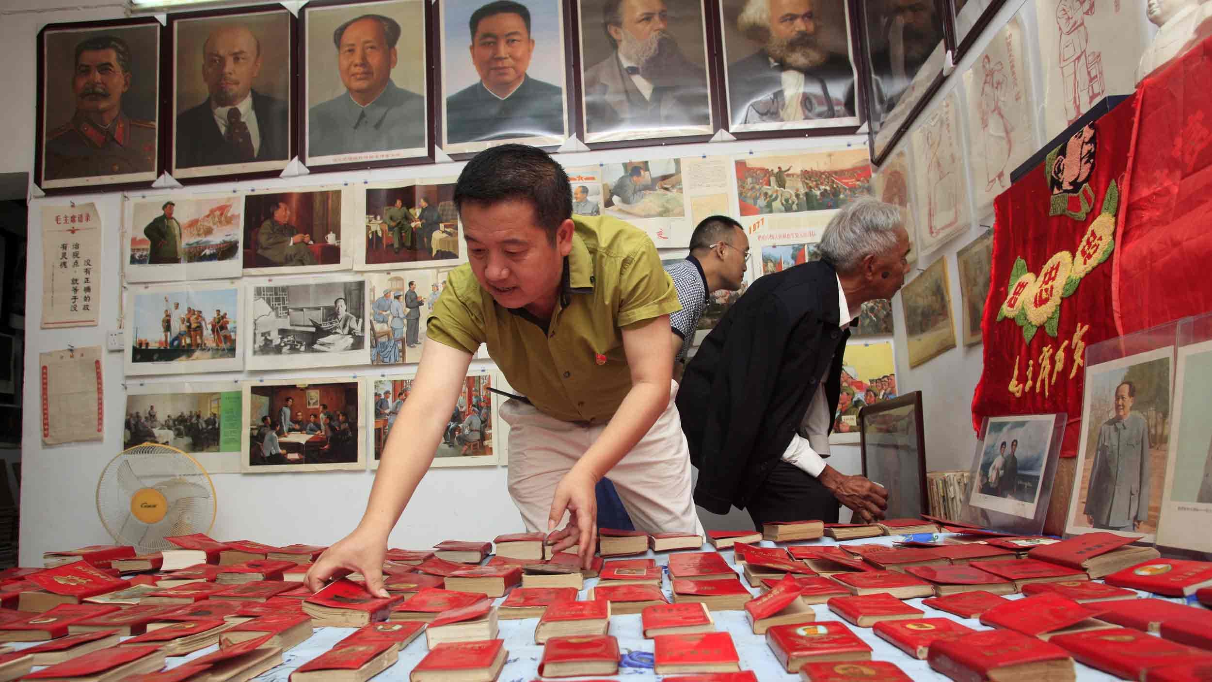 A man leans over a table covered in dozens of identical little red books