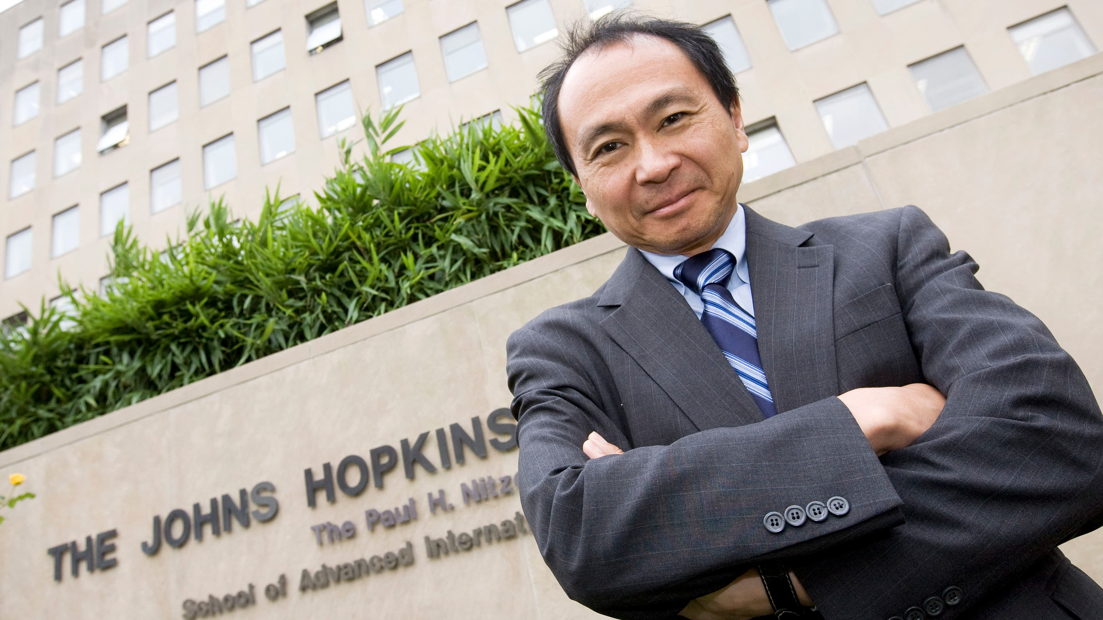 Francis Fukuyama standing outside with his arms crossed.