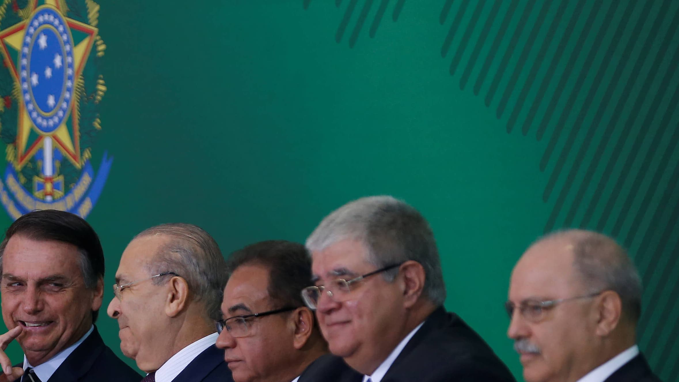 Four men sit in a row in front of a green backdrop.