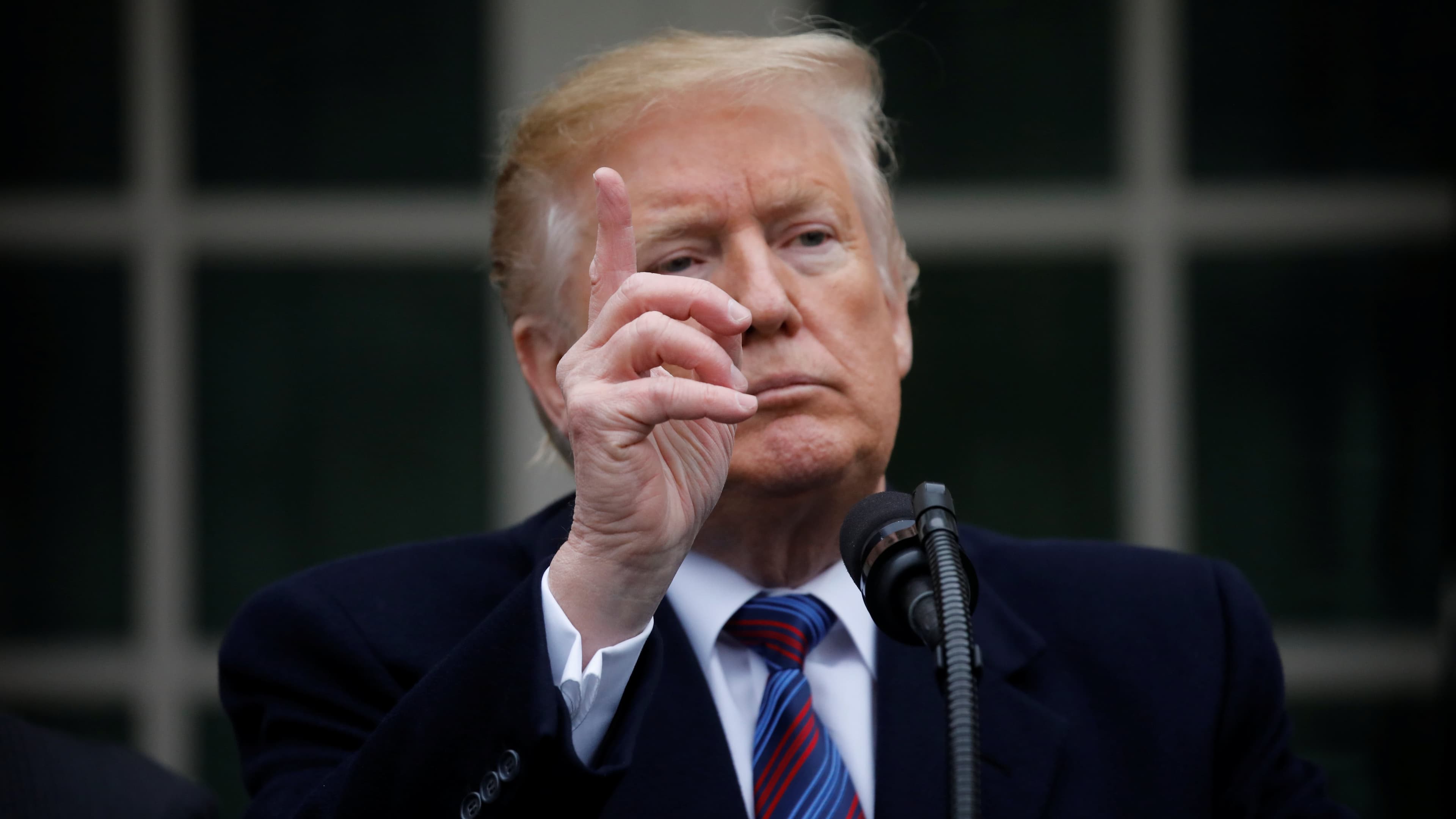 Donald Trump holds up on hand while standing behind a podium