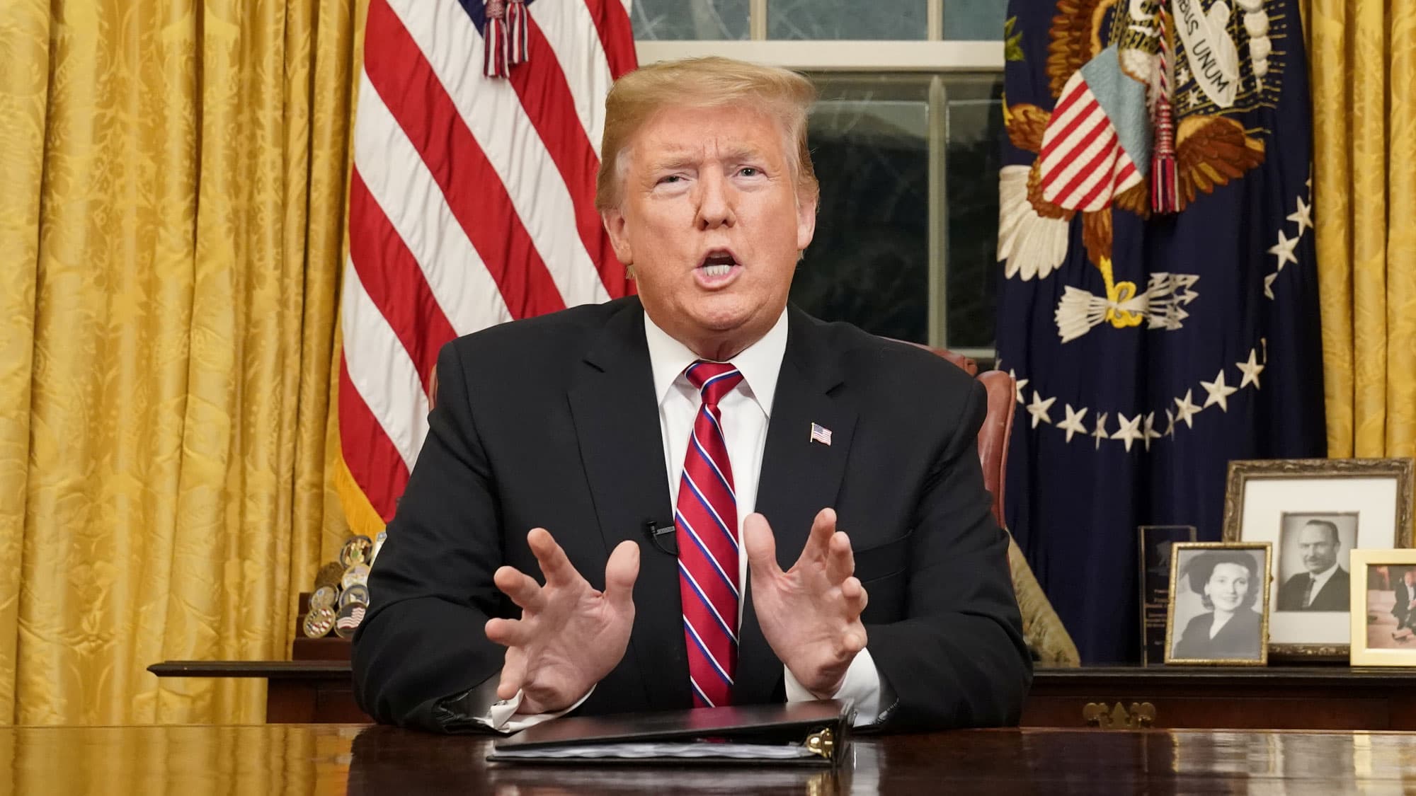 US President Donald Trump is shown seated at a desk with the US flag behind him as he delivers a televised address.