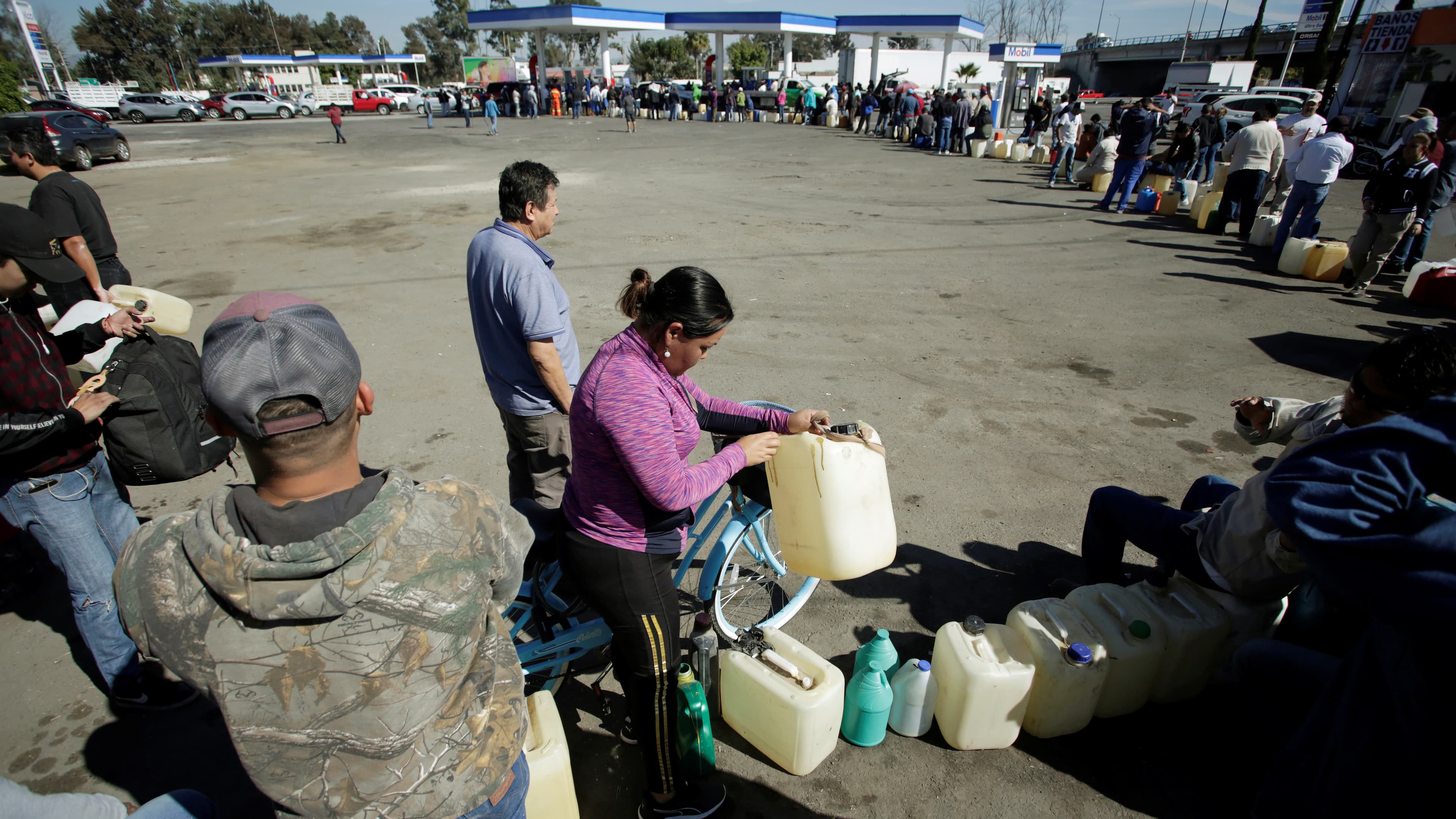hundreds of people stand in line at a gas station on a sunny day