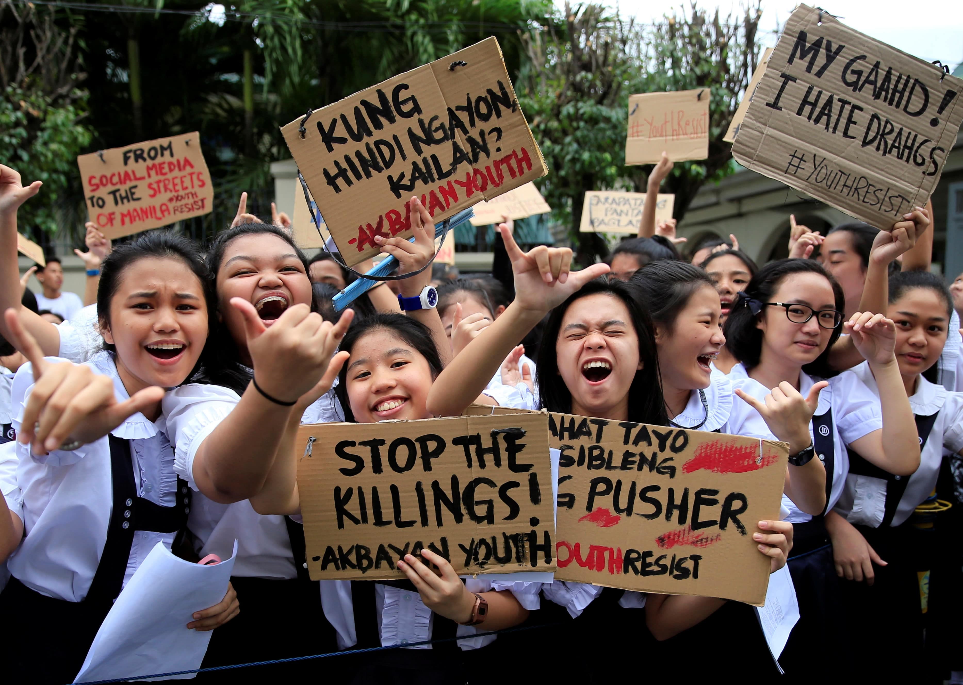 several girls in catholic school uniforms hold signs and chant
