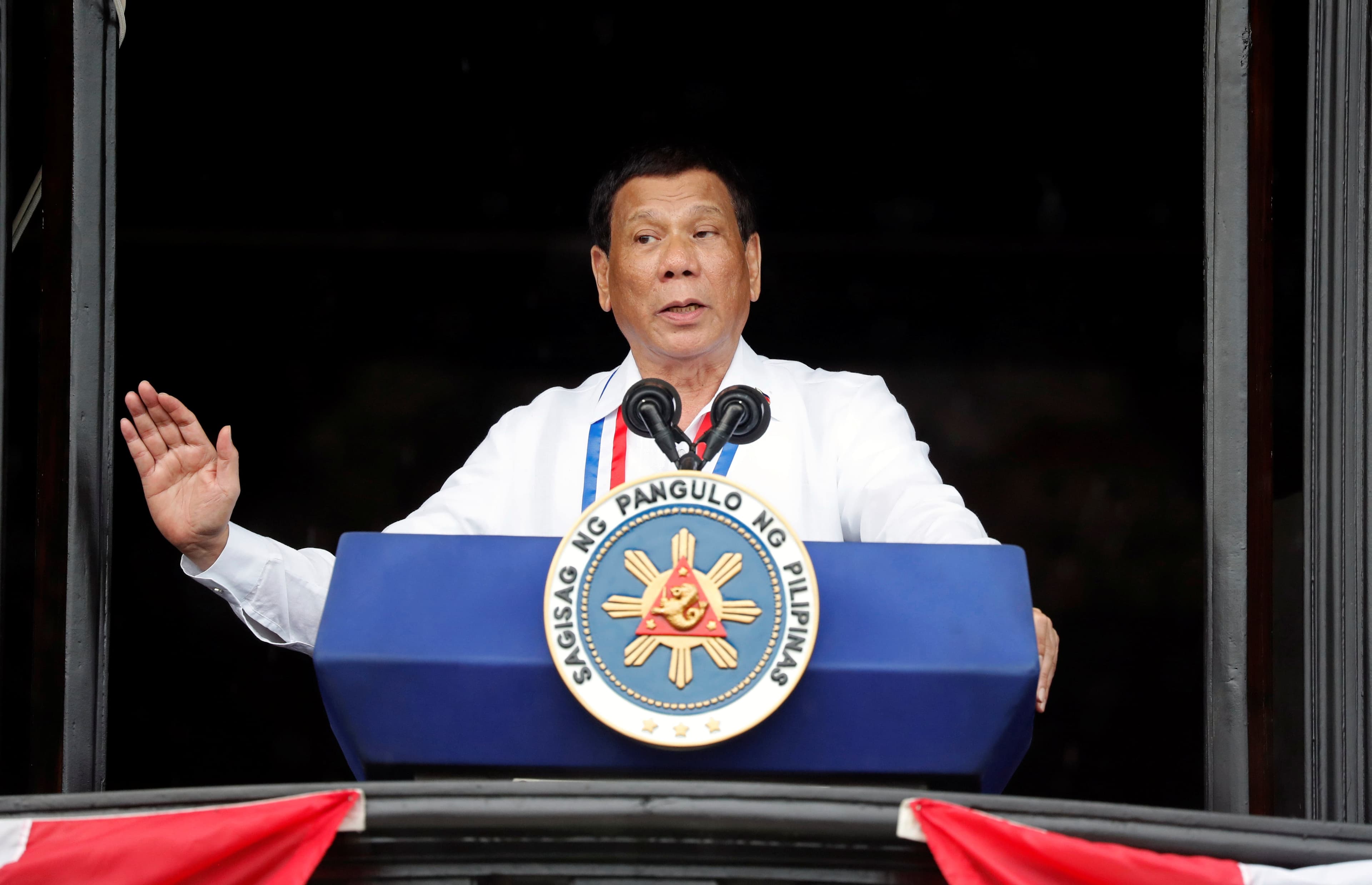 Philippine's President Rodrigo Duterte speaks behind a blue podium in a white shirt
