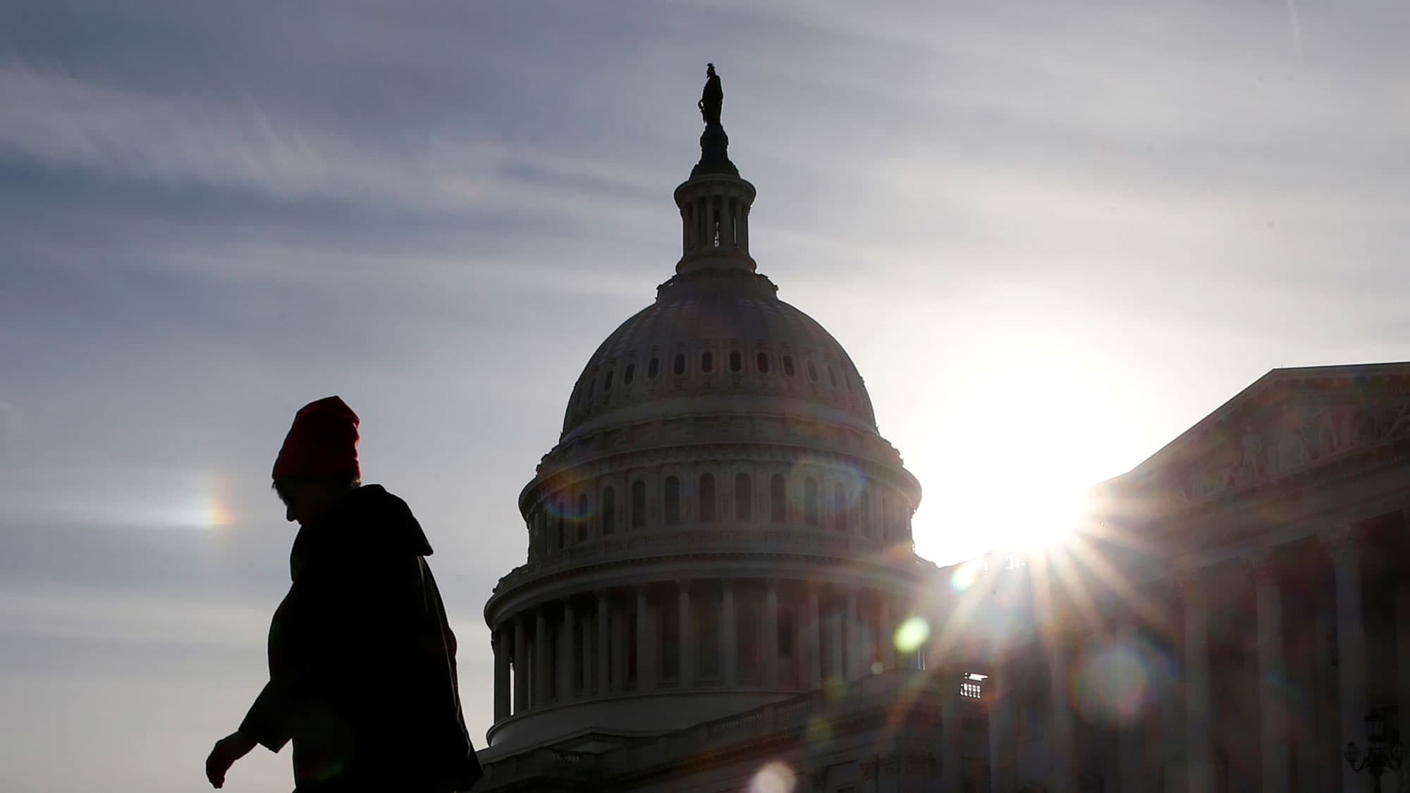 A person is shown in shadow, backlight by a bright sun walking by the US Capitol.