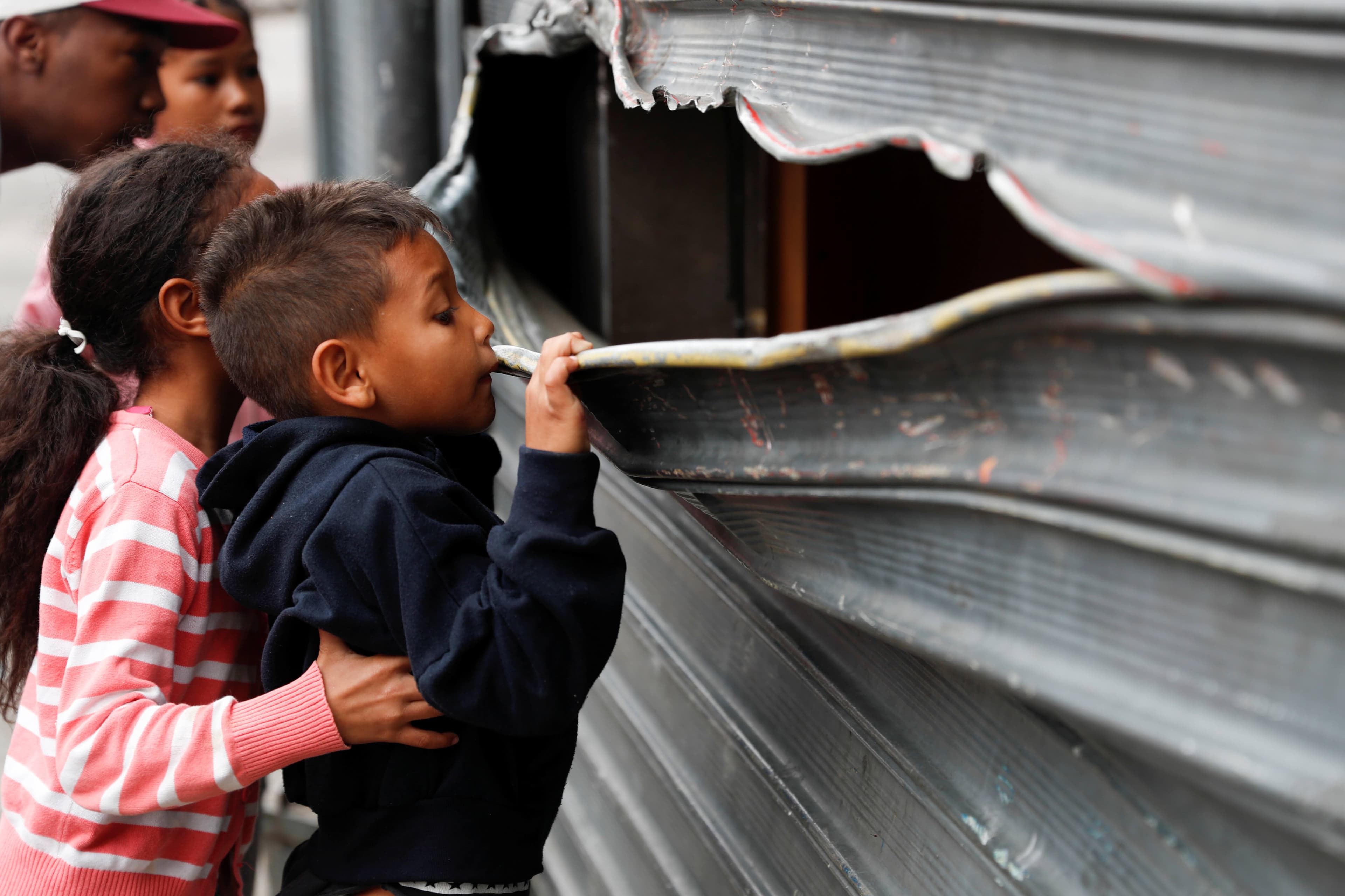 a small boy looks through the bent metal of a garage door