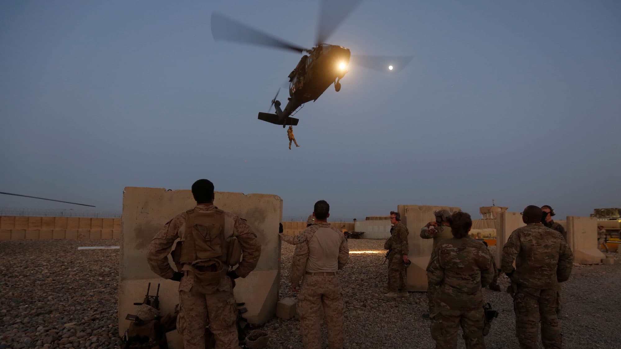 US troops are shown in the near ground with a helicopter flying in the background.