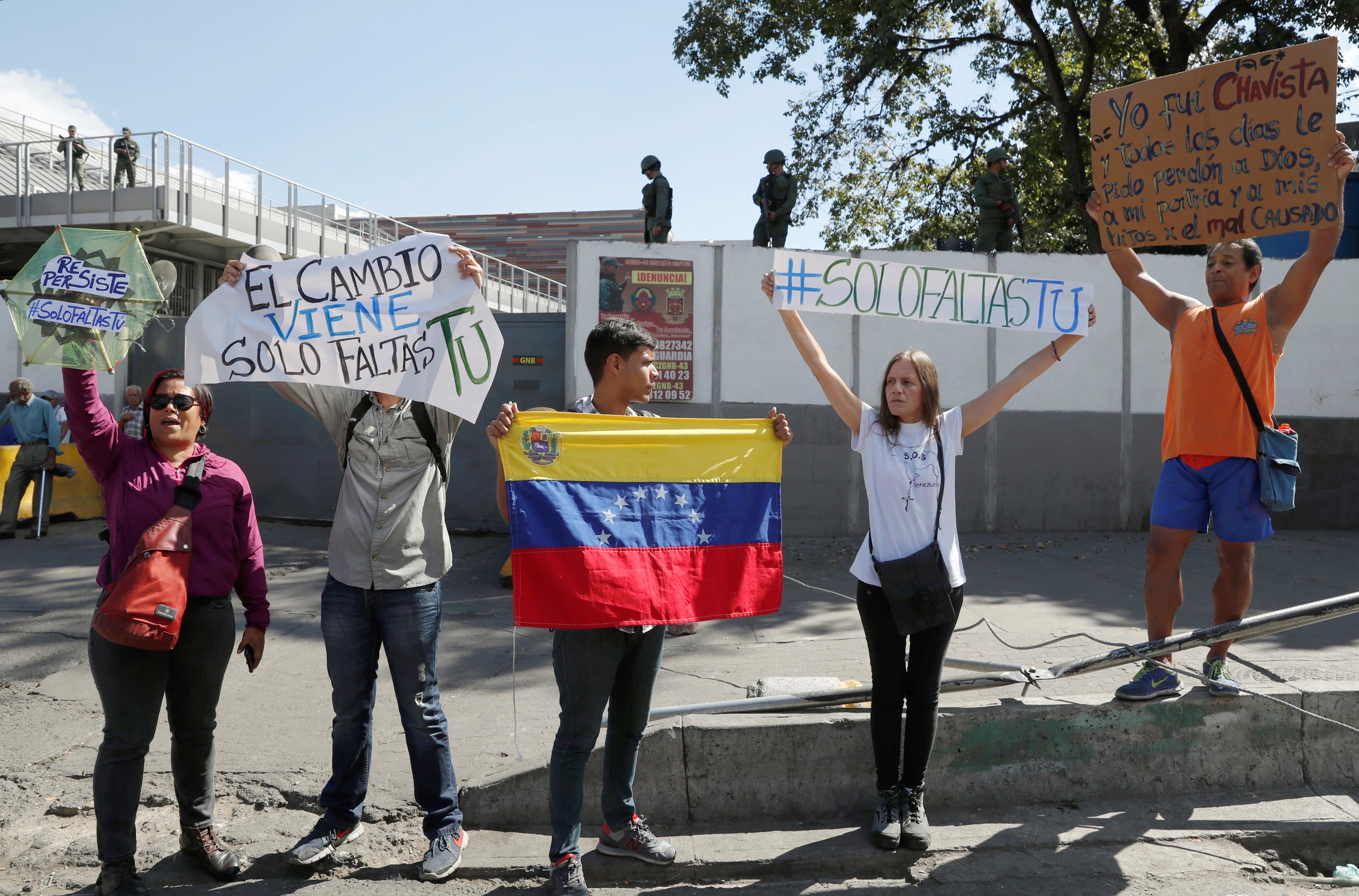 several people hold signs outside the walls of a military outpost