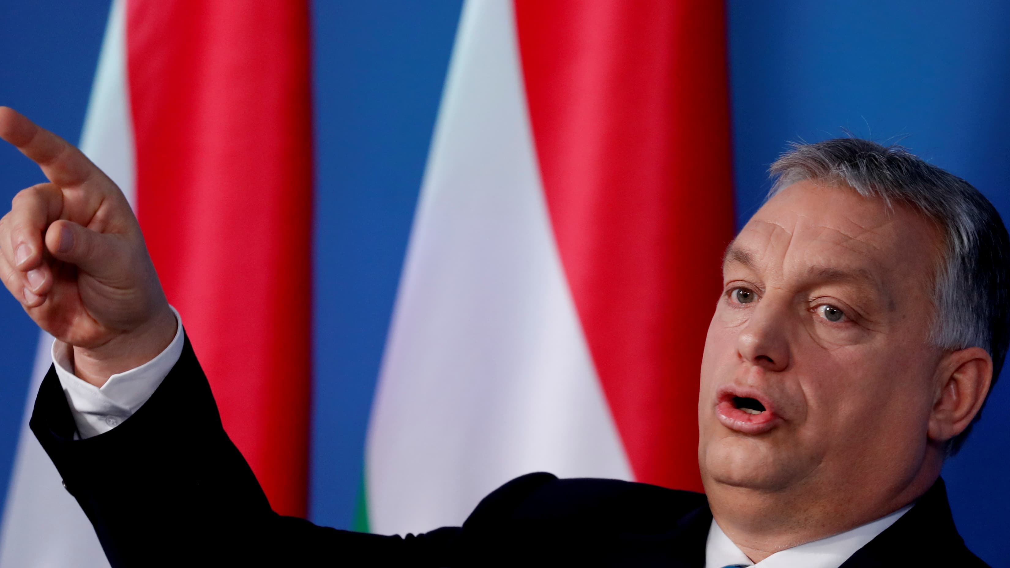 Orban points his finger with red and white flags behind him.