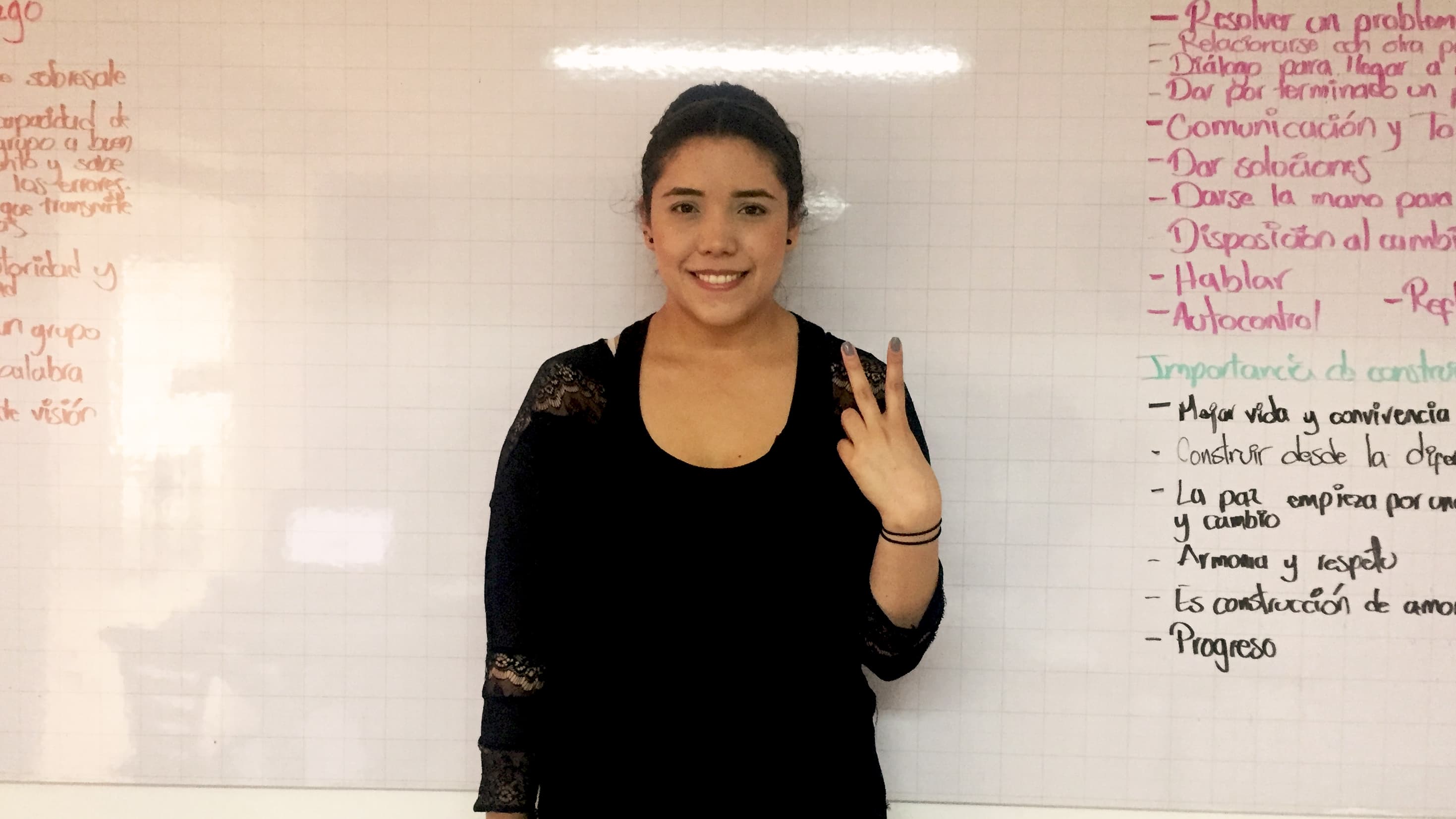 A young woman with dark hair gives the peace sign inside a prison.