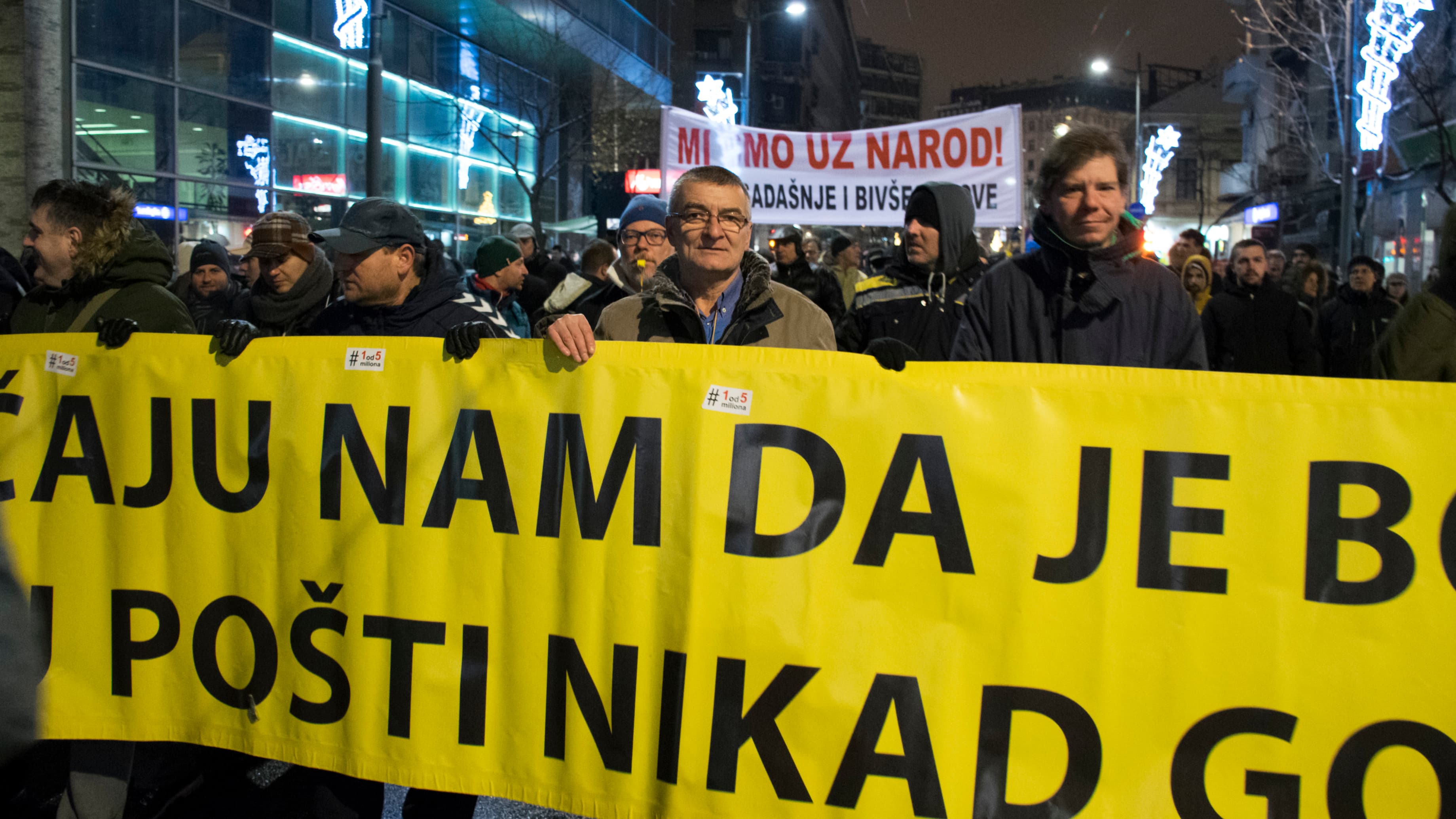 Men carry a huge yellow protest sign with black letters.