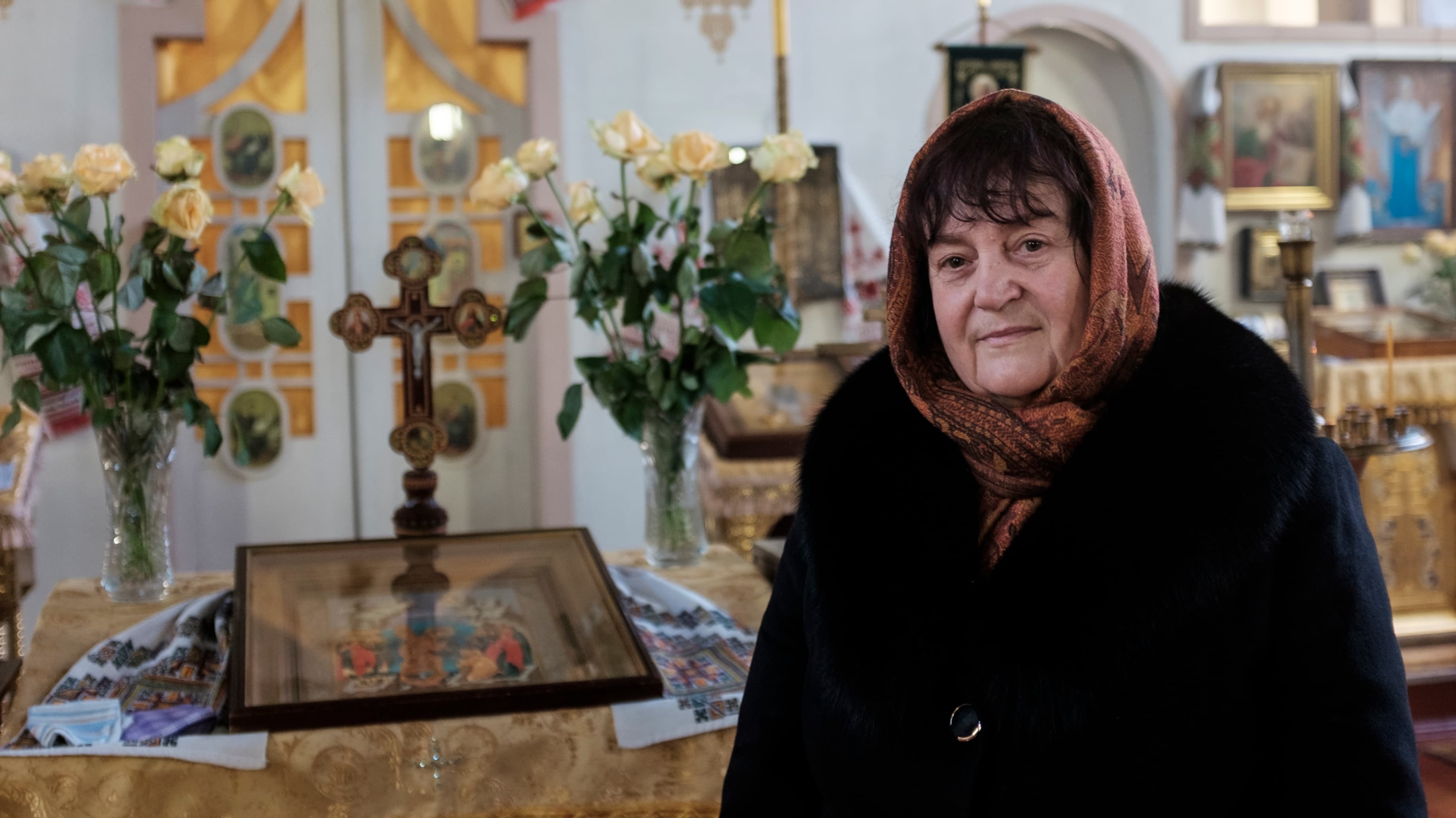 Close up of a woman wearing a head scarf in a church near a gold cross.
