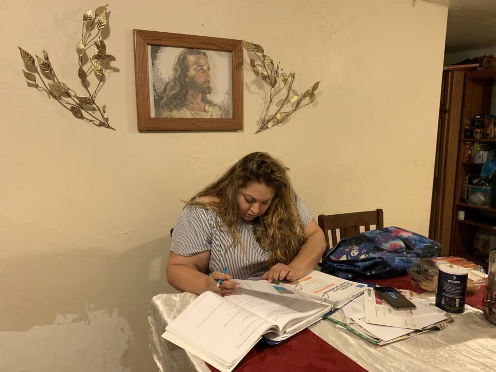 A woman sits at a table, which is field with papers and books