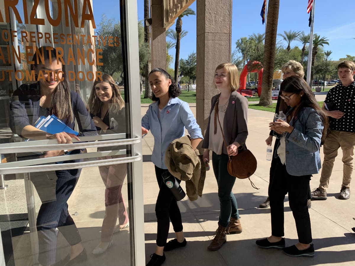 A group of young people walk through a glass door.