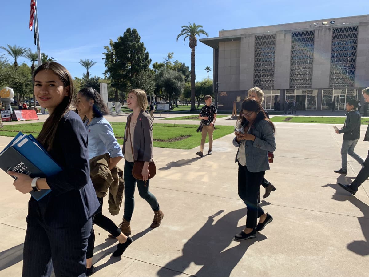 A group of young people walk in front of the Arizona state Capitol.