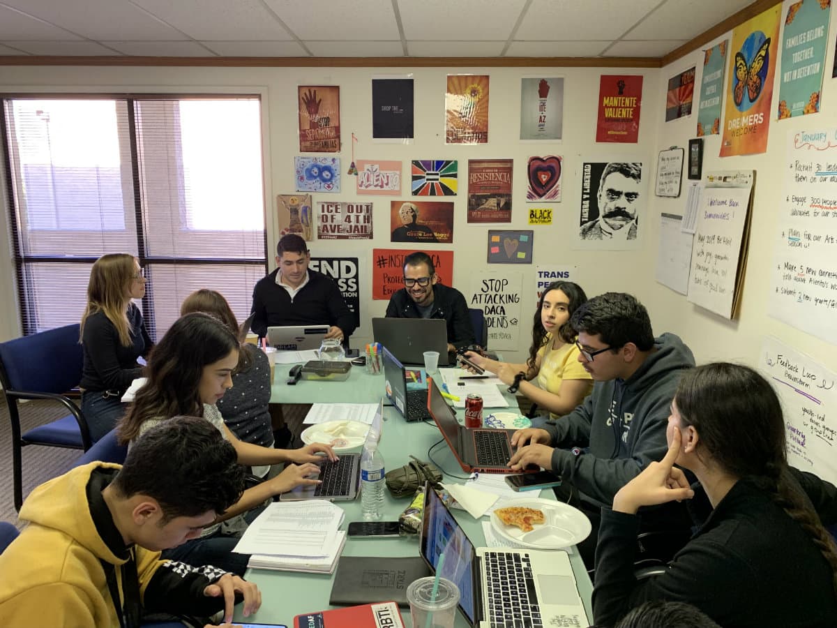 A group of young people sit around a conference table.