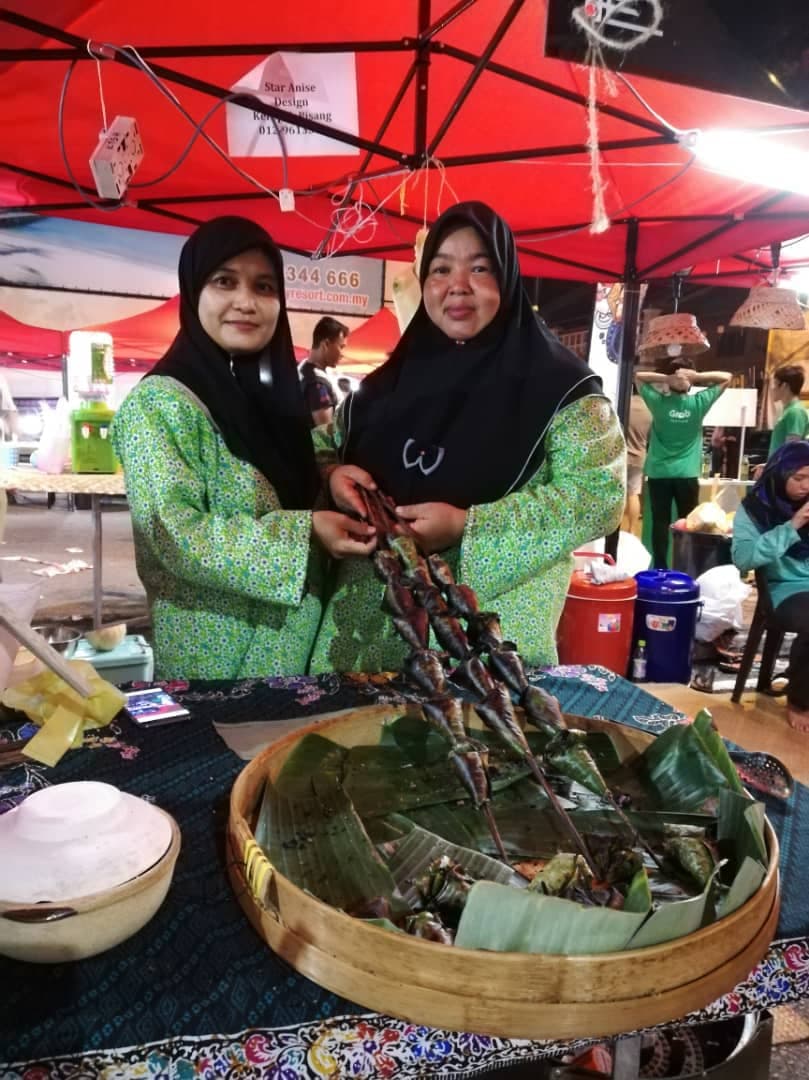 two women wearing head coverings smile under a red awning.