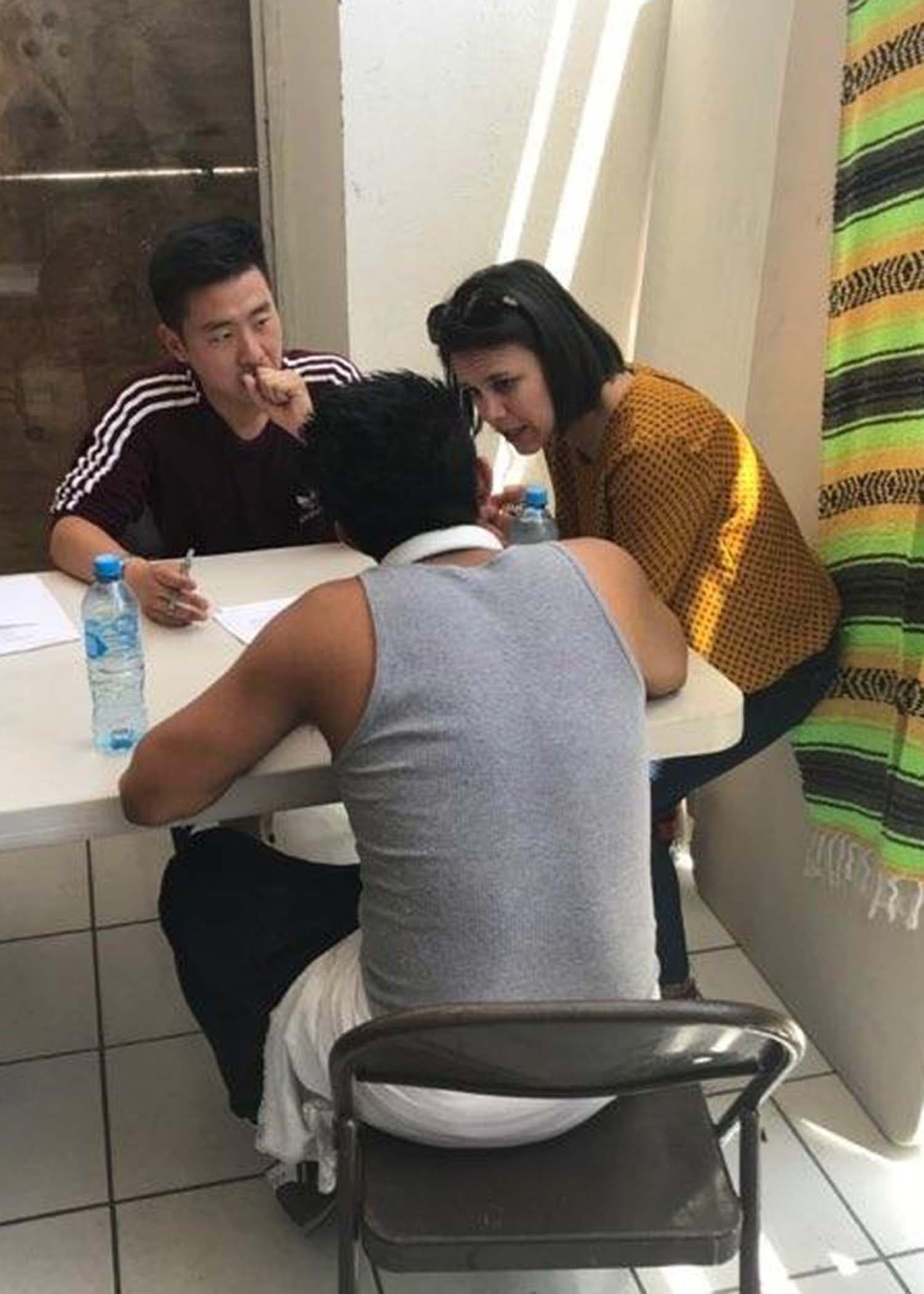 A student sits across from a man at a table. A woman leans at the table.
