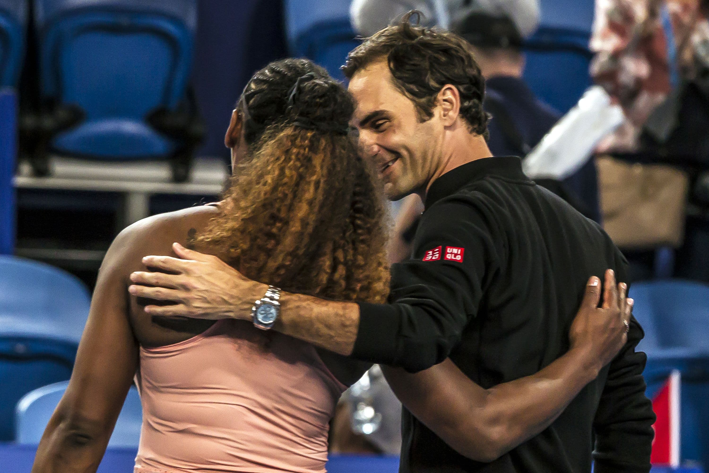 Tennis players Serena Williams and Roger Federer are shown embracing as they walk off the court together.