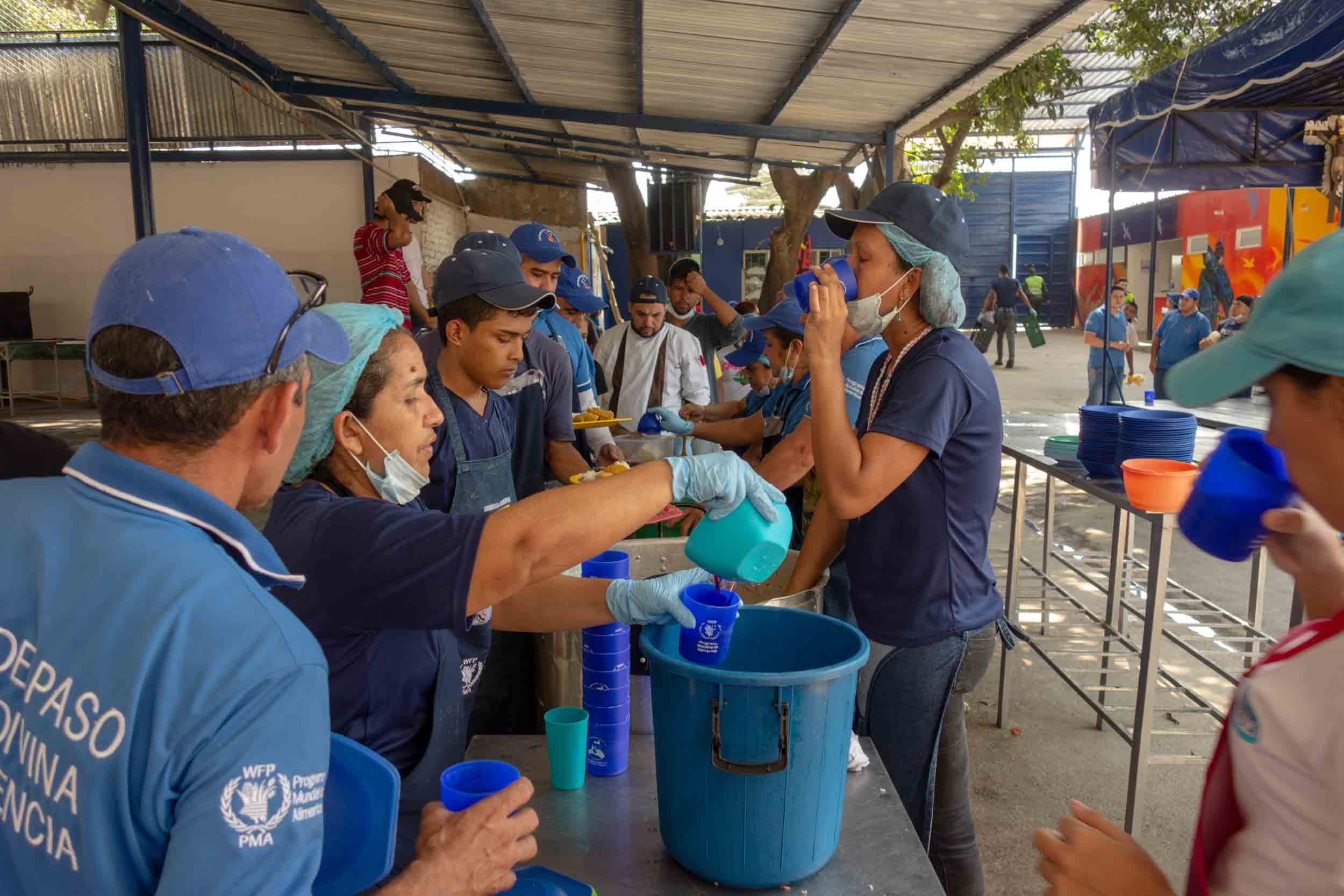 Many people wearing blue shirts stand over pots of food.