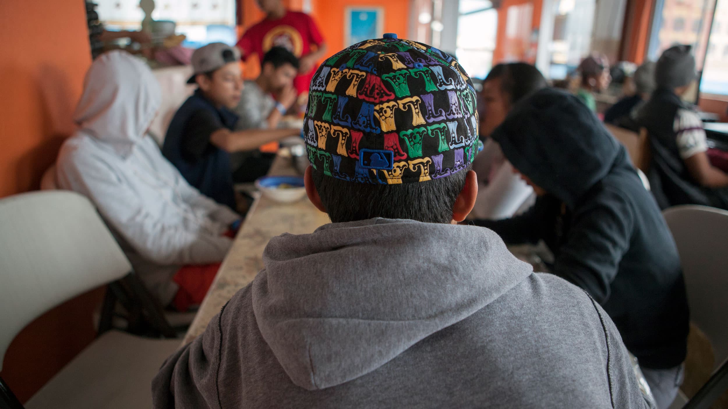 A boy sits with his back to the camera, wearing a baseball cap