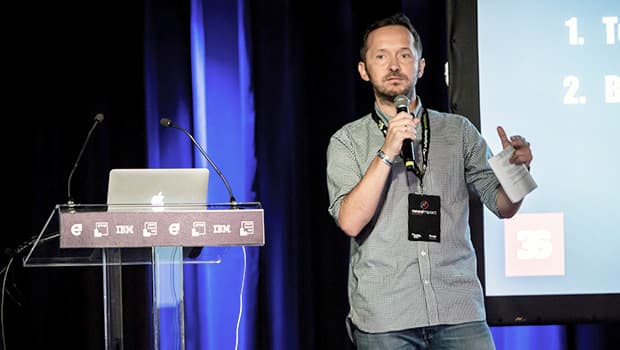 A man holds a microphone and stands in front of a podium on a stage.