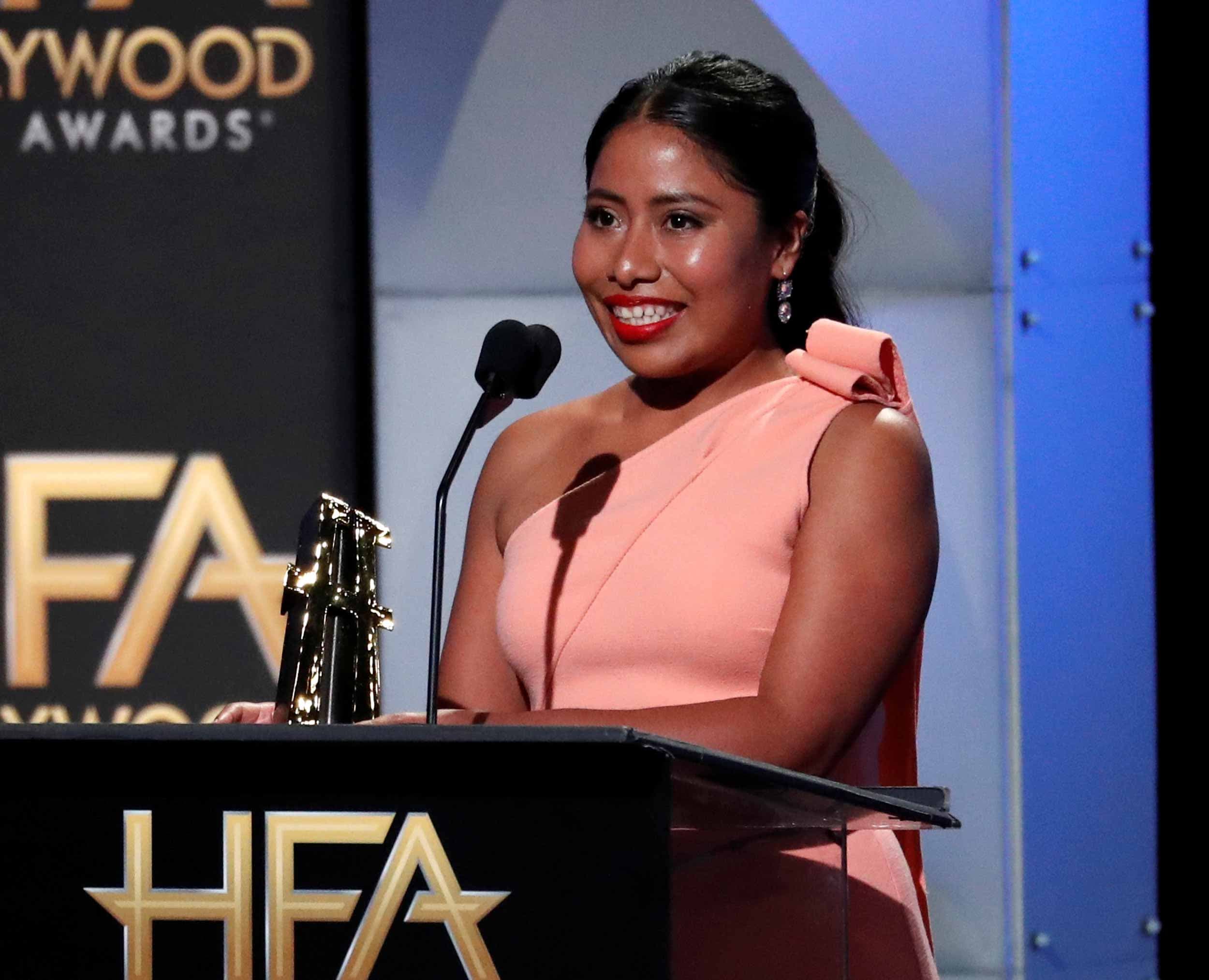 Yalitza Aparicio stands behind a podium holding the New Hollywood Award