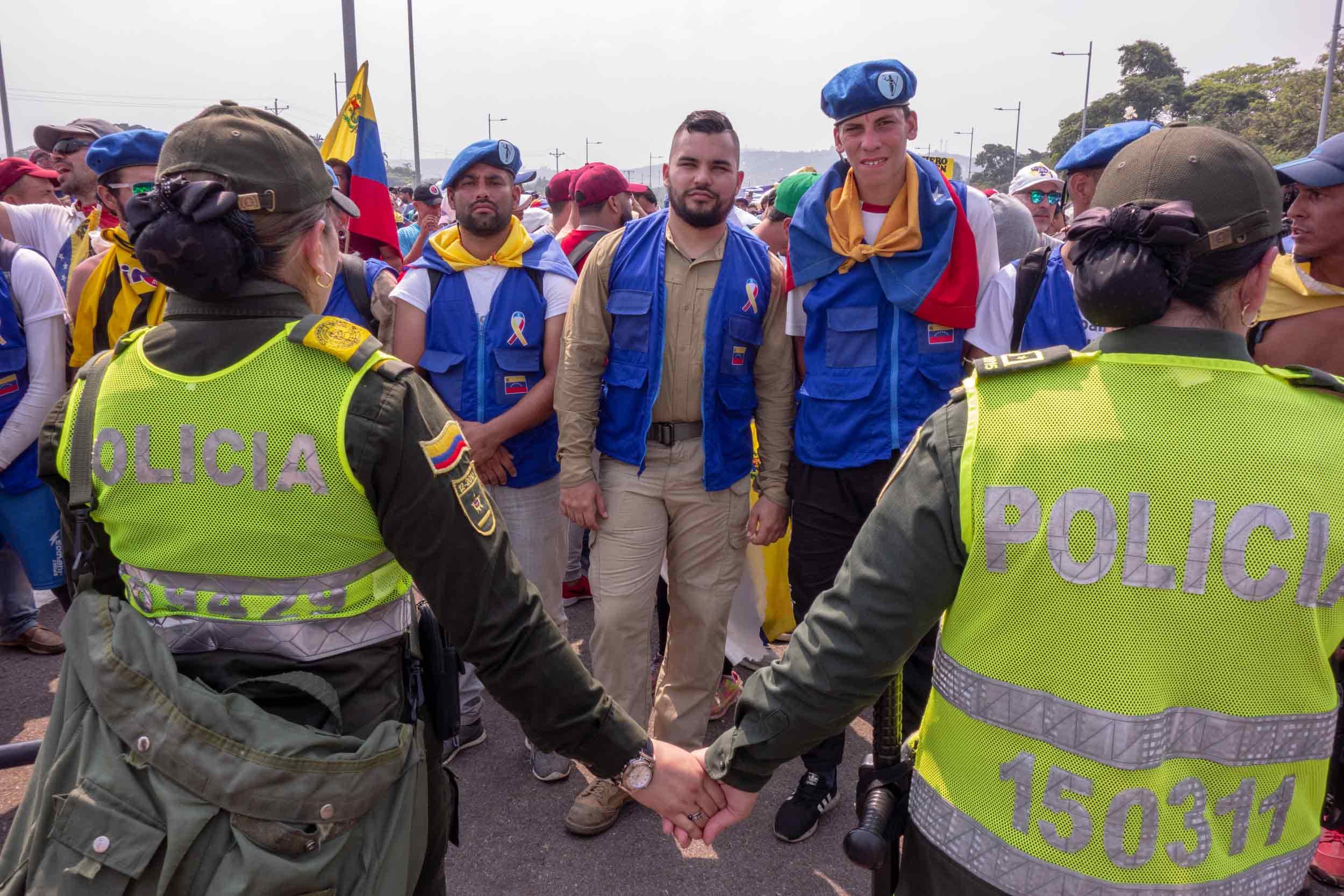 Venezuela volunteers stand in front of Venezuelan police at the border.