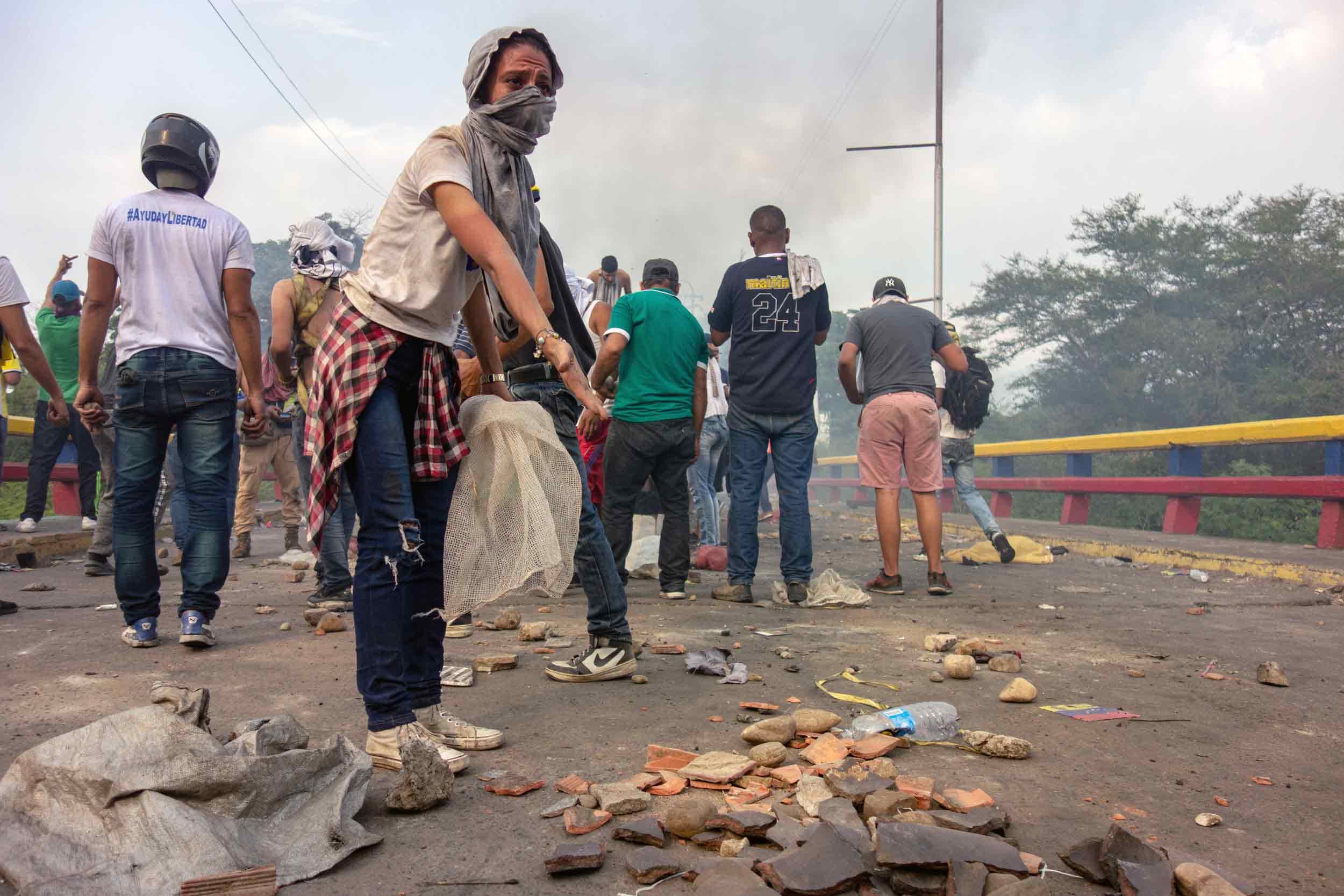A young person wearing a bandana over face throws rock.