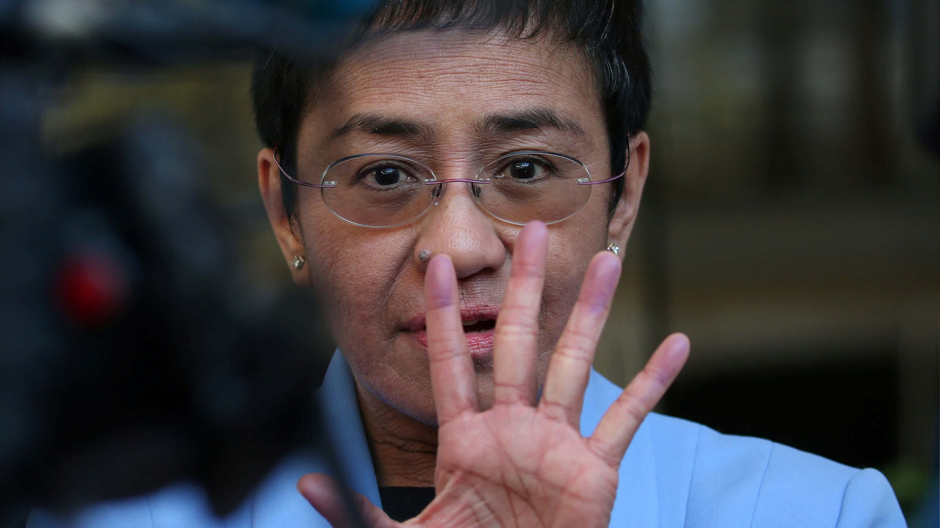 A closeup of Maria Ressa with her hand up in front of her face.